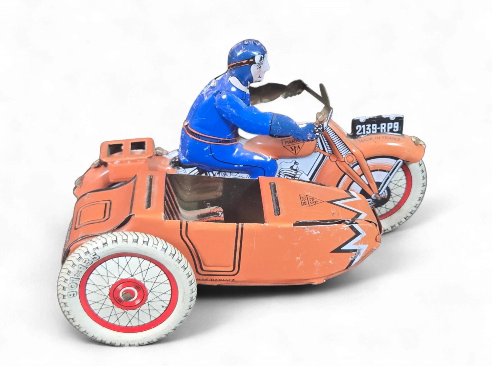 Vintage S.F.A. Paris Lithographed Tinplate Motorcycle with Sidecar and Rider: A vintage S.F.A. Paris lithographed tinplate toy motorcycle with sidecar and rider. The toy depicts an orange motorcycle with an attached sidecar, driven by a blue-suited rider. It features detailed l