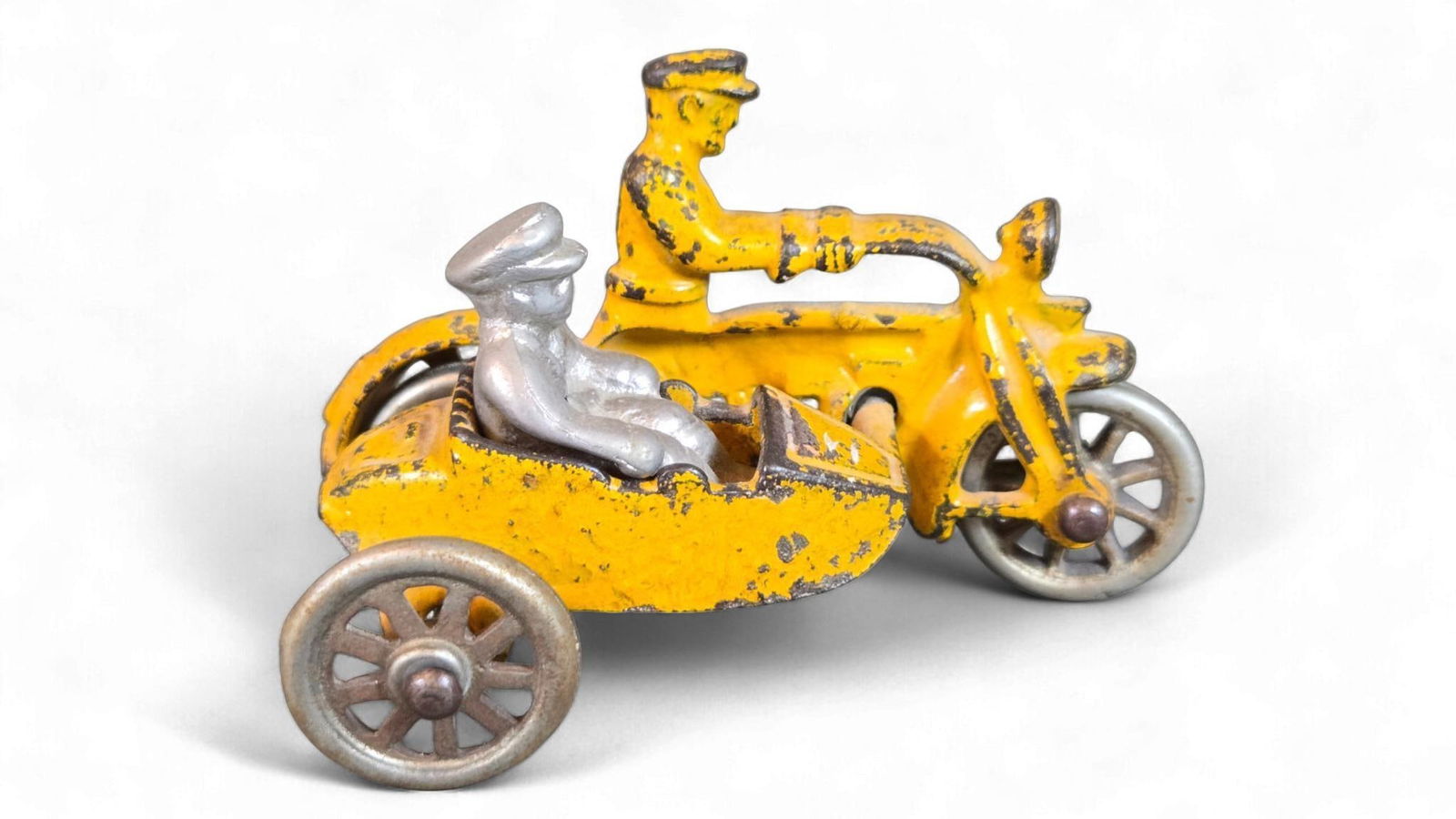 Hubley 1930s Cast Iron Police Motorcycle with Sidecar: A Hubley 1930s cast iron toy, depicting a police motorcycle with an attached sidecar. The main body of the motorcycle and the driver figure are painted yellow. A separate, unpainted silver-colored fig