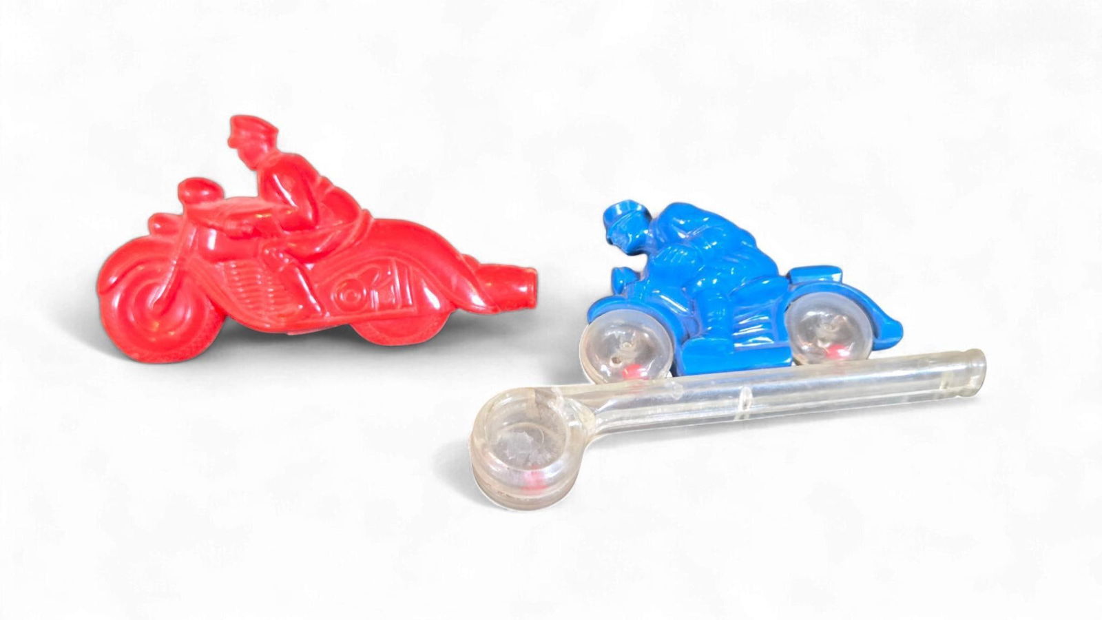 Two 1950s Commonwealth Plastics Corp. Plastic Motorcycle Whistles: A group of two 1950s plastic whistles, two attributed to Commonwealth Plastics Corp. The lot comprises two toy motorcycles with integrated riders and a clear plastic tube whistle. The red motorcycle f