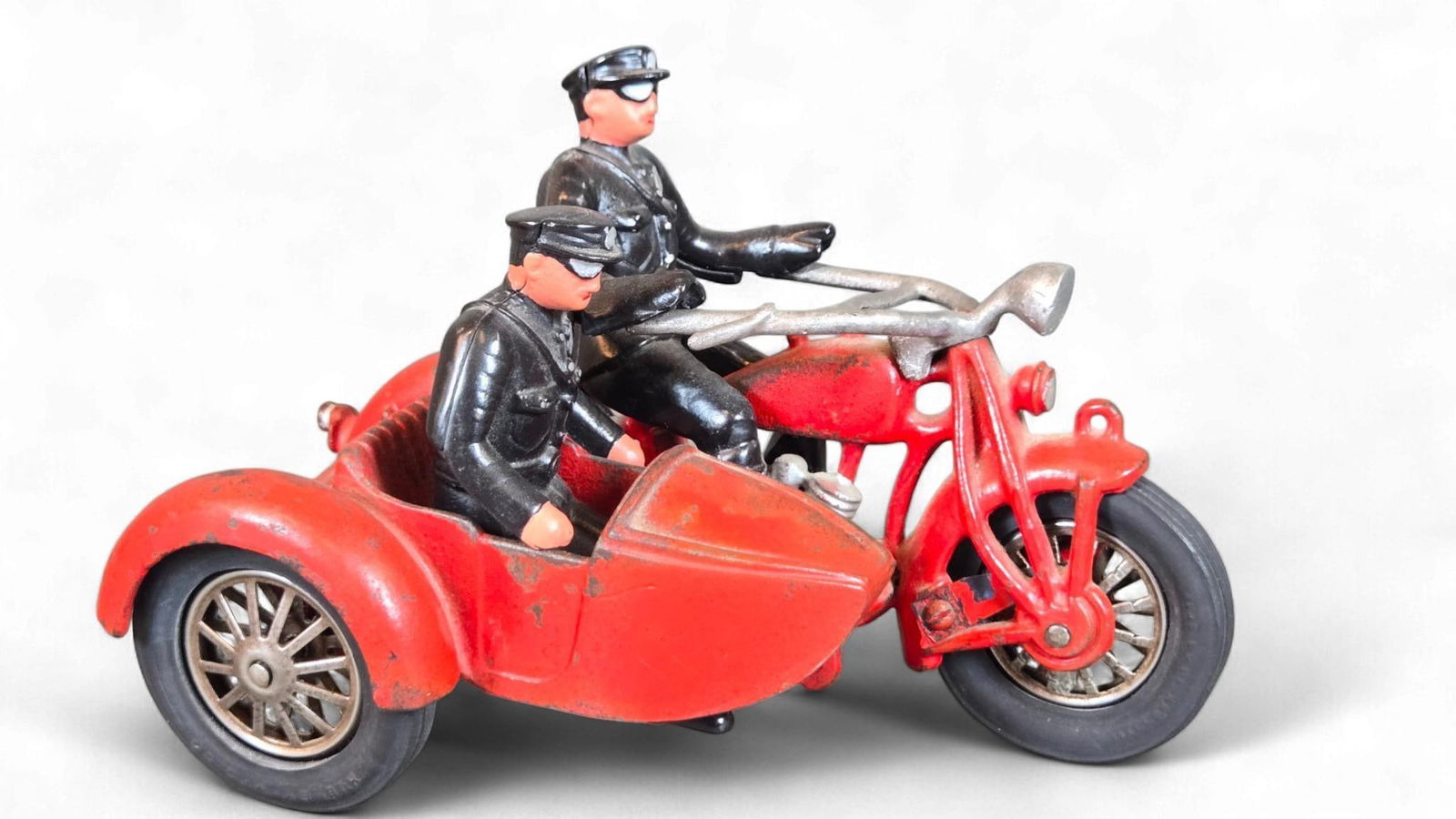 A Hubley Cast Iron Indian Police Motorcycle with Sidecar, circa 1930s: A Hubley Cast Iron Indian Police Motorcycle with Sidecar, circa 1930s. This vintage toy is primarily constructed from cast iron with rubber tires. The motorcycle and sidecar are painted a vibrant red,