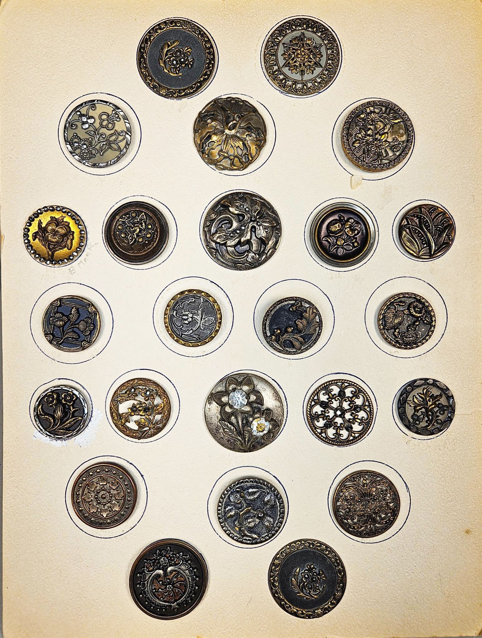 A Collection of Victorian and Art Nouveau Style Mixed Metal Buttons: A group of antique or vintage buttons, primarily circular and crafted from a variety of metals including brass, bronze, and silver-toned alloys, some accented with dark enamel or oxidized finishes. Th
