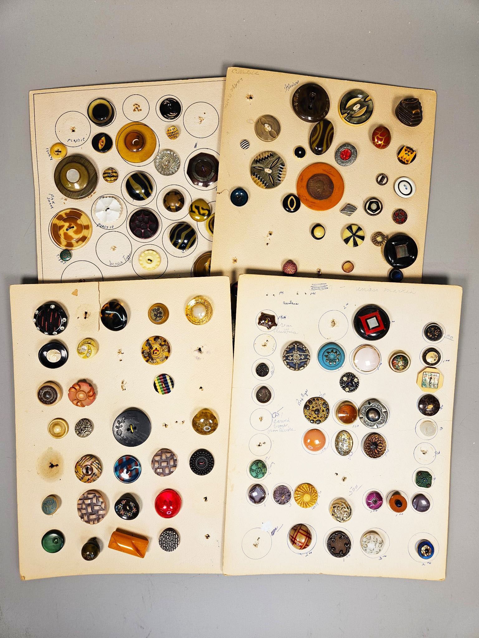 A Large Collection of Vintage Buttons, Including Bakelite, Celluloid, Carved Bone, Metal, Glass, and: A large collection of vintage buttons, meticulously arranged and displayed on group of aged paper cards. The buttons exhibit a wide array of styles, ranging from Art Deco-inspired geometric patterns,