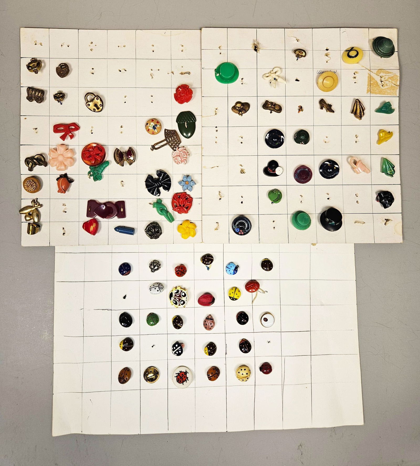 A Collection of Late 20th Century 'Realistics' Buttons and Charms: A collection of miniature decorative objects, primarily buttons and charms, dating from the late 20th century. The lot comprises numerous items displayed across group of grid-lined cardboard sheets, f