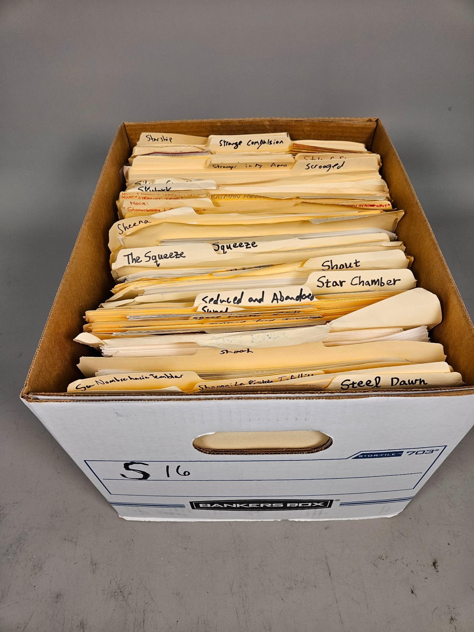 A Collection of Film Publicity Photographs and Archives, 1970s-1980s: A collection of black and white film publicity photographs and associated manila file folders, housed within a cardboard Bankers Box (labeled "S16" and "STOR-FILE 703"). The photographs are primarily