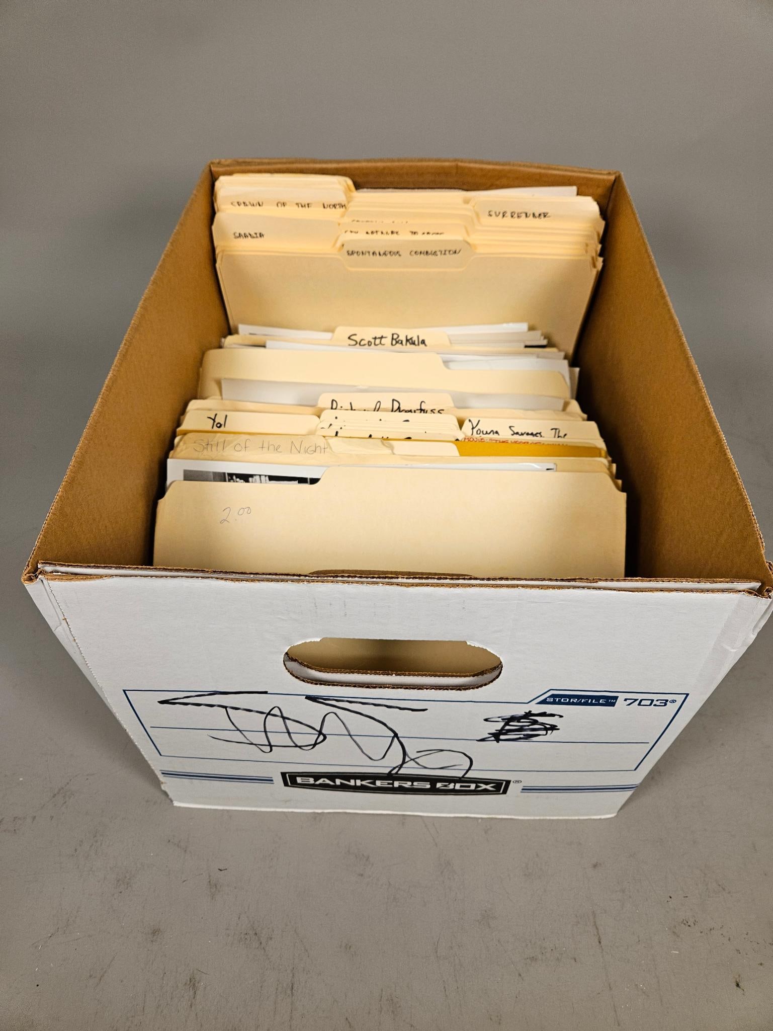A Collection of Film and Television Production Stills and Archival Material in a Bankers Box: A brown cardboard Bankers Box, model "STOR/FILE 703," containing a collection of manila file folders and numerous photographic prints. The folders are labeled with handwritten English titles, includin