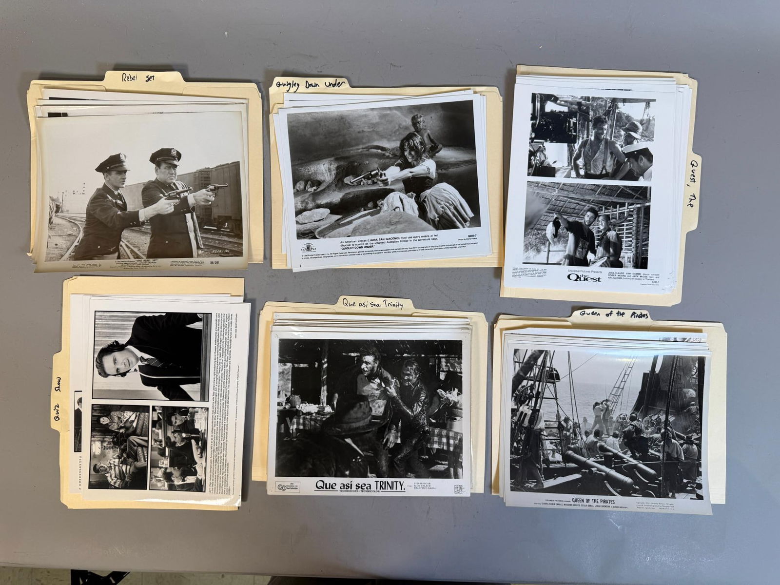 A Collection of Vintage Black and White Film and Television Press Stills, circa 1960s-1990s: A collection of black and white photographic press stills, primarily 8x10 inches with white borders, organized within labeled manila file folders. The folders are titled "Rebel Set," "Quigley Down Und