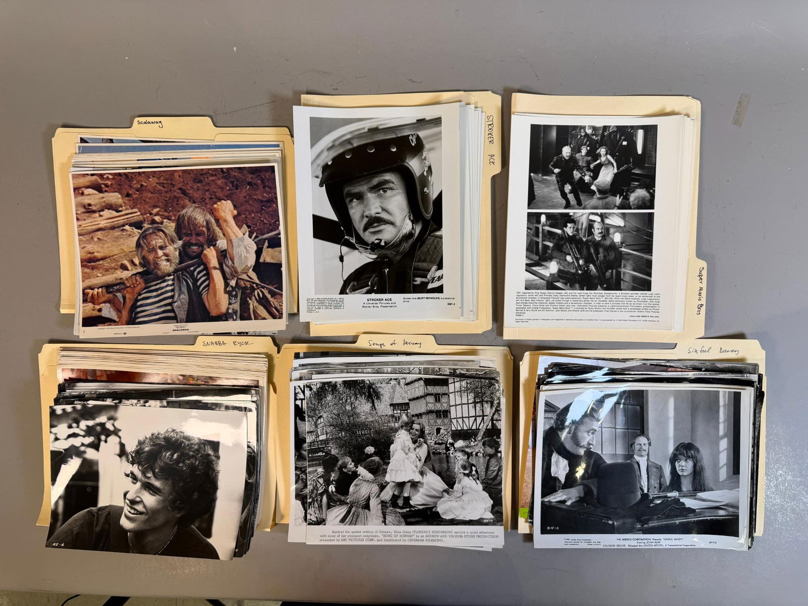 A Collection of Vintage Film Publicity Photographs, including 'Stroker Ace', 'Super Mario Bros', and: This lot comprises a collection of vintage film publicity photographs, primarily 8x10-inch glossy prints, housed in labeled yellow manila folders. The collection includes a mix of both black and white