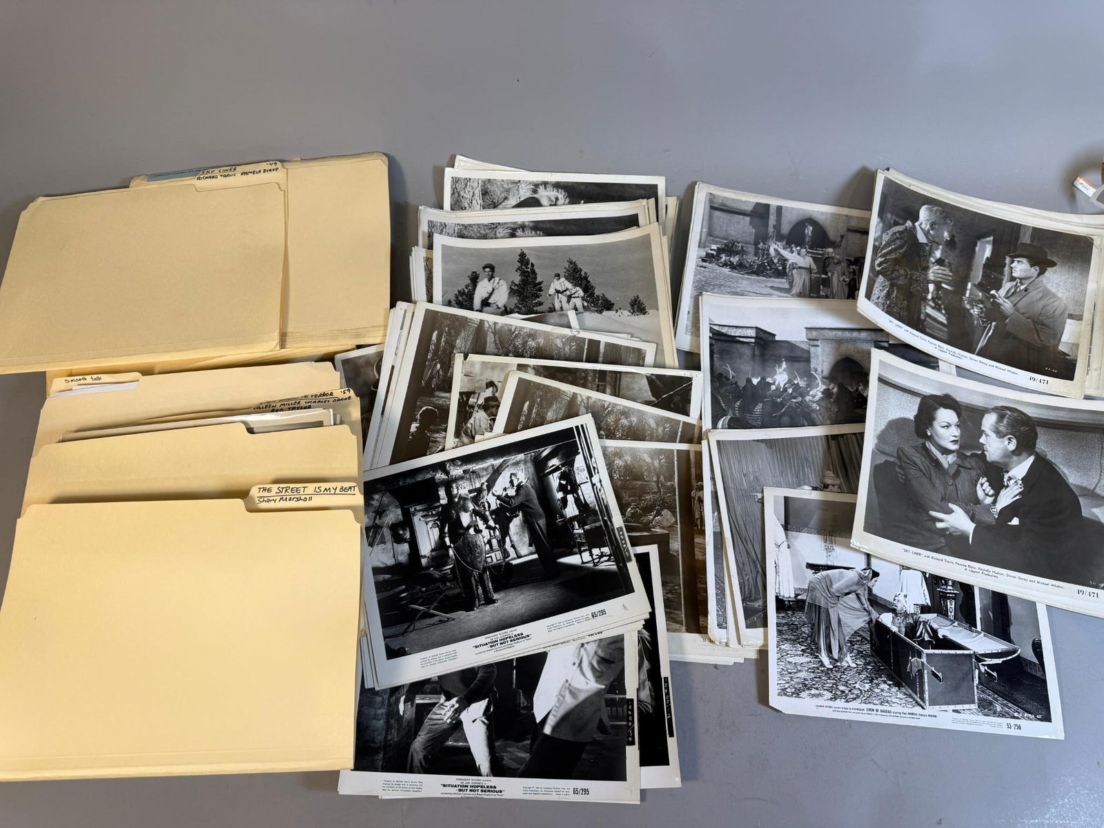 A Collection of Black and White Film and Television Publicity Stills, 1940s-1970s: A large collection of black and white photographic prints, primarily movie stills and publicity photos, accompanied by several labeled manila file folders. The prints, many featuring attached paper ca