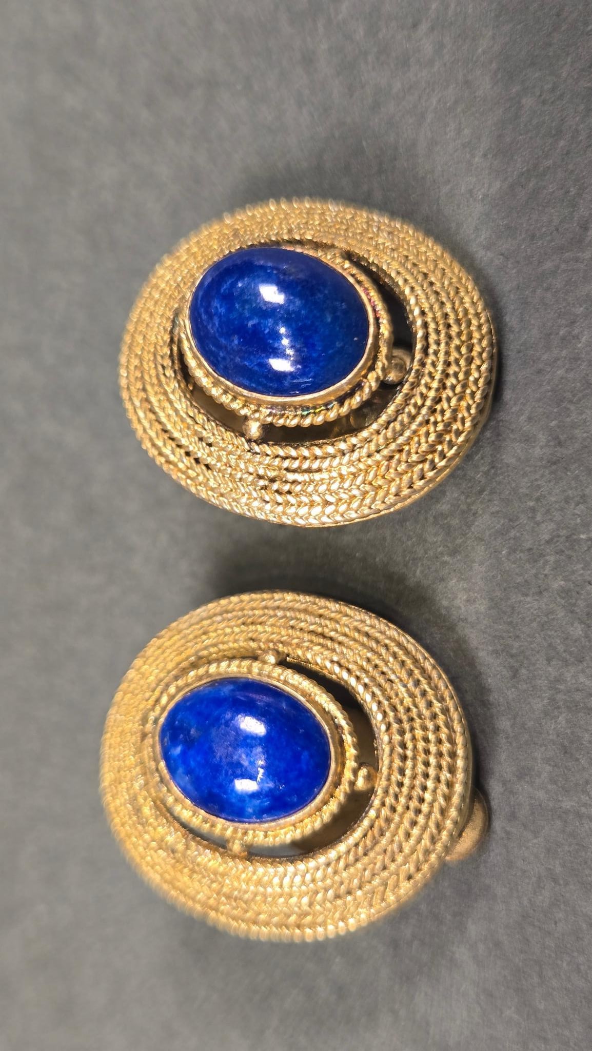 A Pair of Gold-Toned Sterling Silver and Lapis Lazuli Clip-On Earrings: A pair of circular clip-on earrings, crafted from Sterling Silver and featuring a gold-toned braided or rope-textured border. Each earring is centered with an oval, domed lapis lazuli cabochon. The re