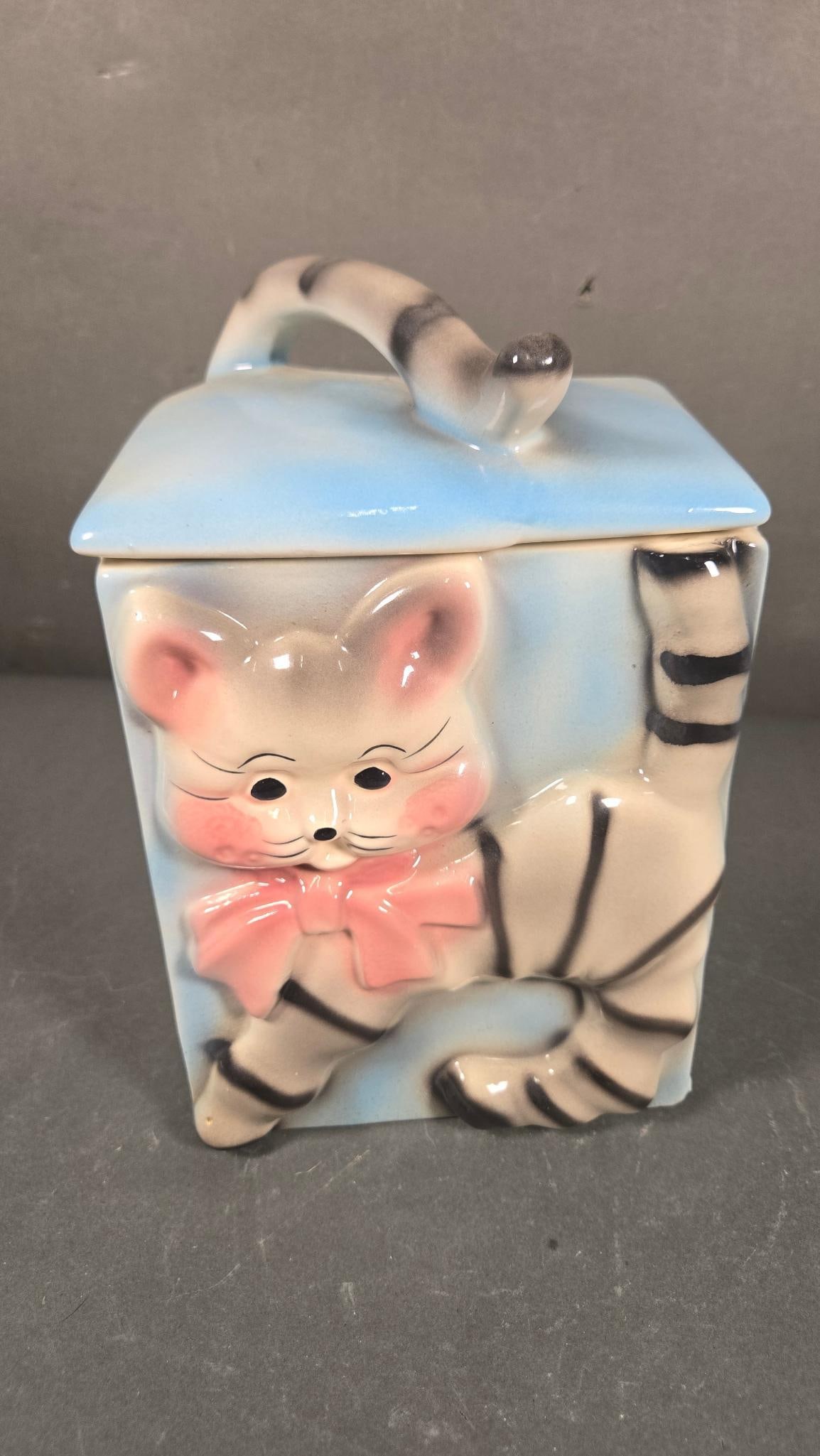 American Bisque Cat Cookie Jar with Tail Lid Handle, circa 1950s: An American Bisque glazed ceramic lidded jar, commonly known as a 'Cat Cookie Jar with Tail Lid Handle'. The jar features a whimsical, light blue rectangular body adorned with a three-dimensional anth