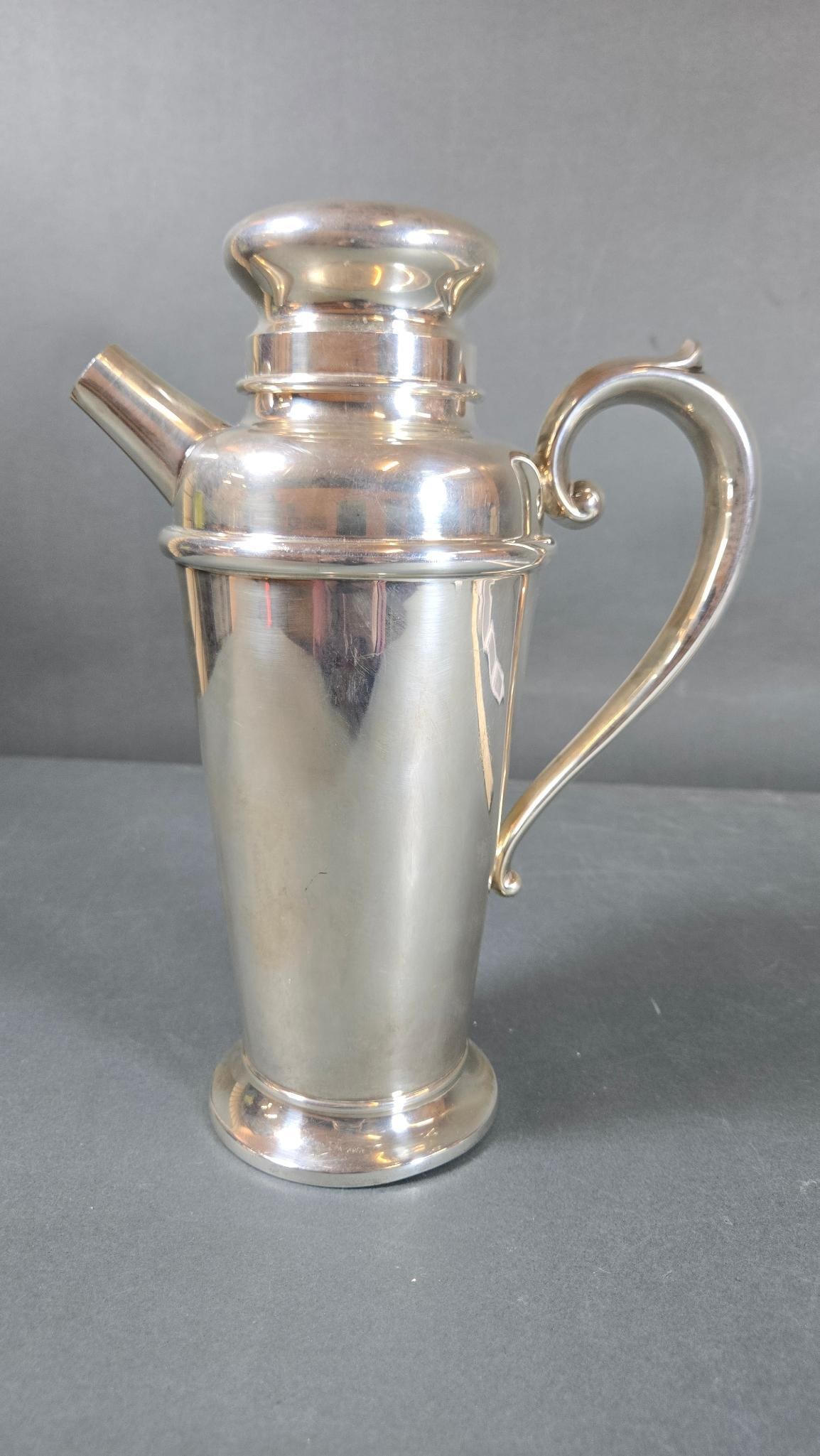 A Vintage .835 Silver Cocktail Shaker by Watson & Co.: A vintage .835 fineness silver cocktail shaker by Watson & Co. The shaker features a tapered body, a curved handle, a short spout, and a multi-part lid with a removable cap, exhibiting a classic, util
