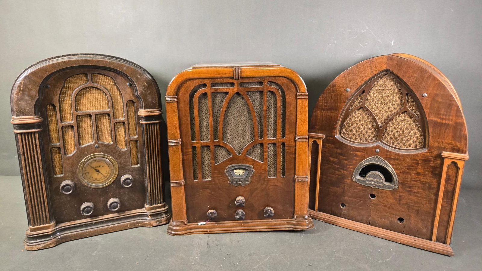Three Vintage Radios: A Stewart-Warner R-110-A (1934) and Two Atwater Kent Tombstone Radios,: A group of three vintage "tombstone" or "cathedral" style cabinet radios, all exhibiting Art Deco design elements consistent with the 1930s era. Each is primarily constructed from wood, likely veneere