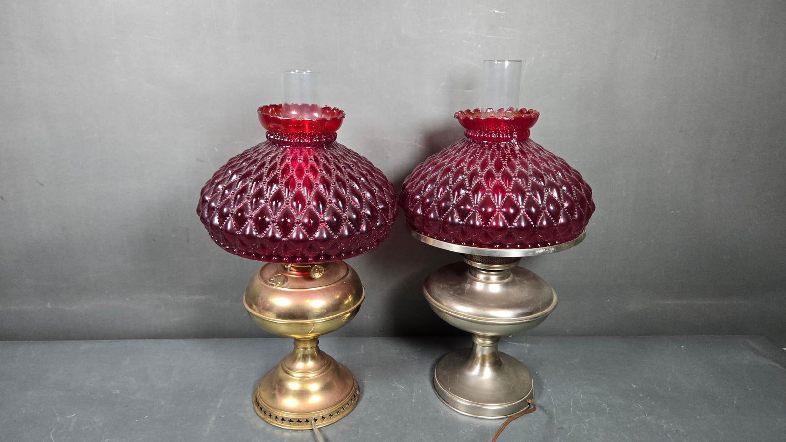 A Pair of Electrified Ruby Red Diamond Quilted 'Gone with the Wind' Style Lamps: A pair of electrified ruby red diamond quilted 'Gone with the Wind' style lamps, featuring distinct metal bases and matching ruby-red, diamond-quilted glass shades with ruffled rims, topped by clear g