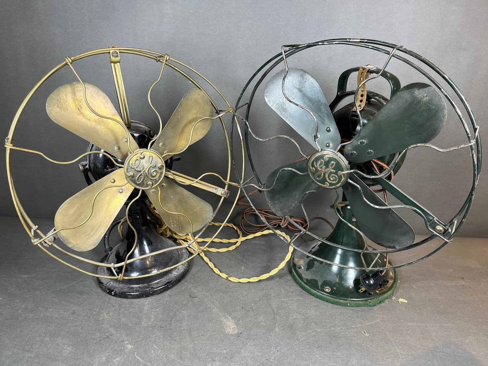 A Pair of General Electric Early 20th-Century Oscillating Desk Fans: A pair of General Electric oscillating desk fans, exhibiting an early 20th-century industrial style. Both fans feature a cast iron base and motor housing, a four-blade propeller, and a wire safety cag