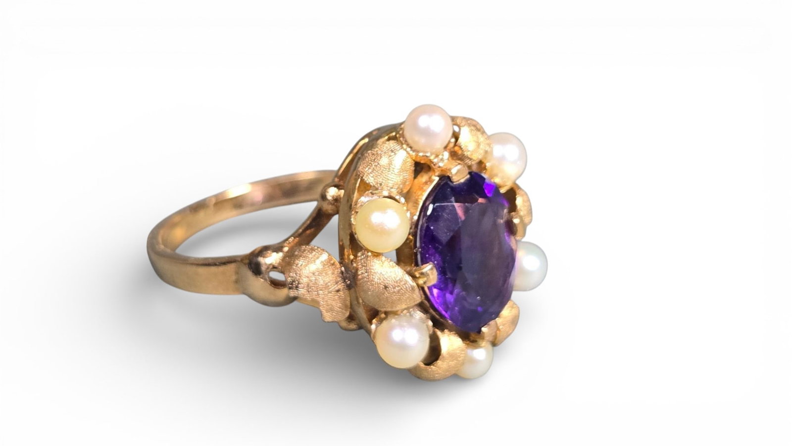 A 19th Century 14k Gold, Amethyst, and Pearl Ring: A 19th-century ring crafted from 14k gold, featuring a central faceted oval amethyst, surrounded by a cluster of small round pearls and delicate textured gold leaf-like motifs, set on a plain polished