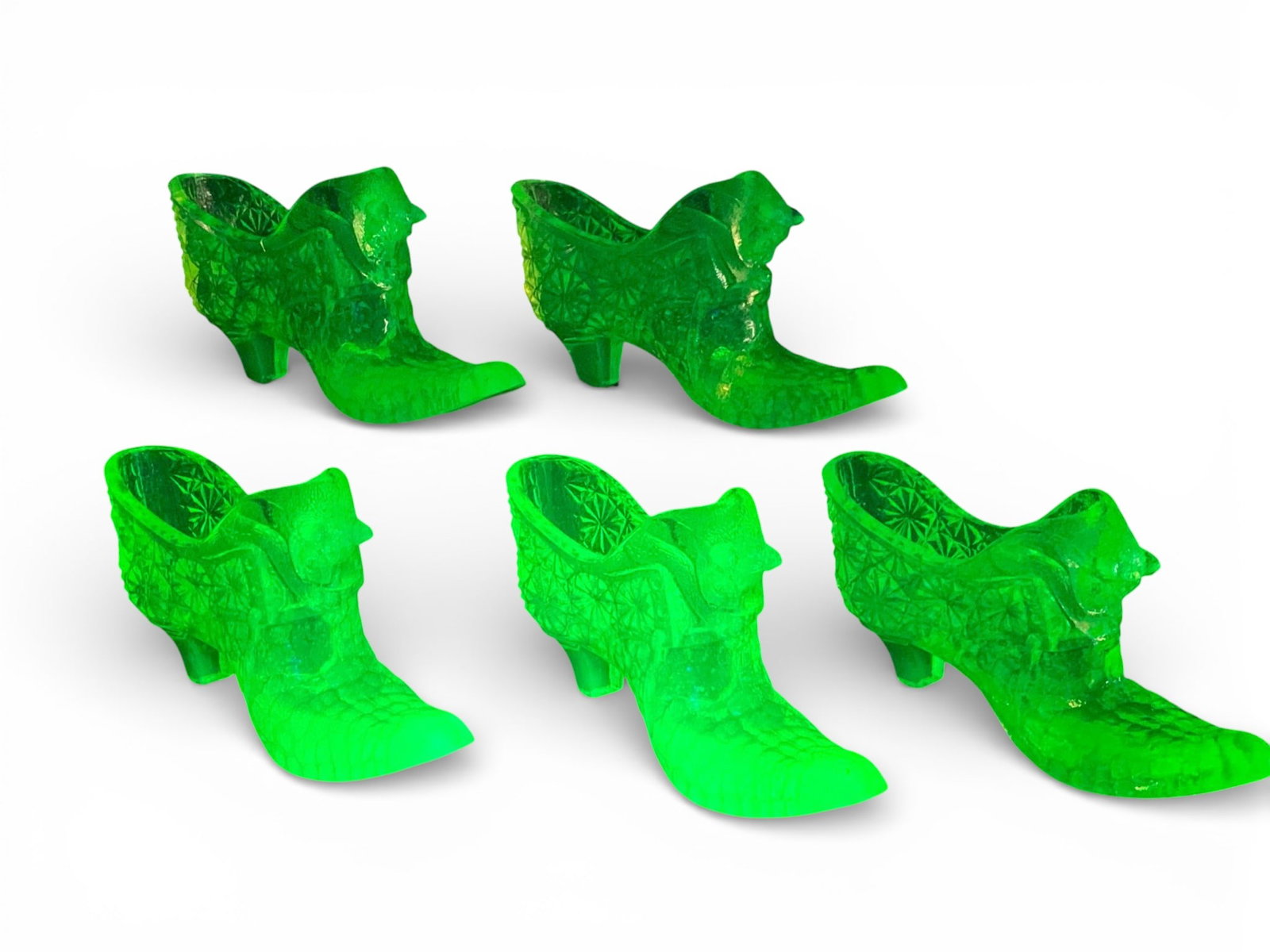 A Collection of Degenhart Cat Head Novelty Boots in Uranium Vaseline Glass: A collection of novelty figural boots attributed to Degenhart Glass, executed in translucent uranium (Vaseline) pressed glass. Each boot features a pointed toe, a low heel, and is decorated with geome