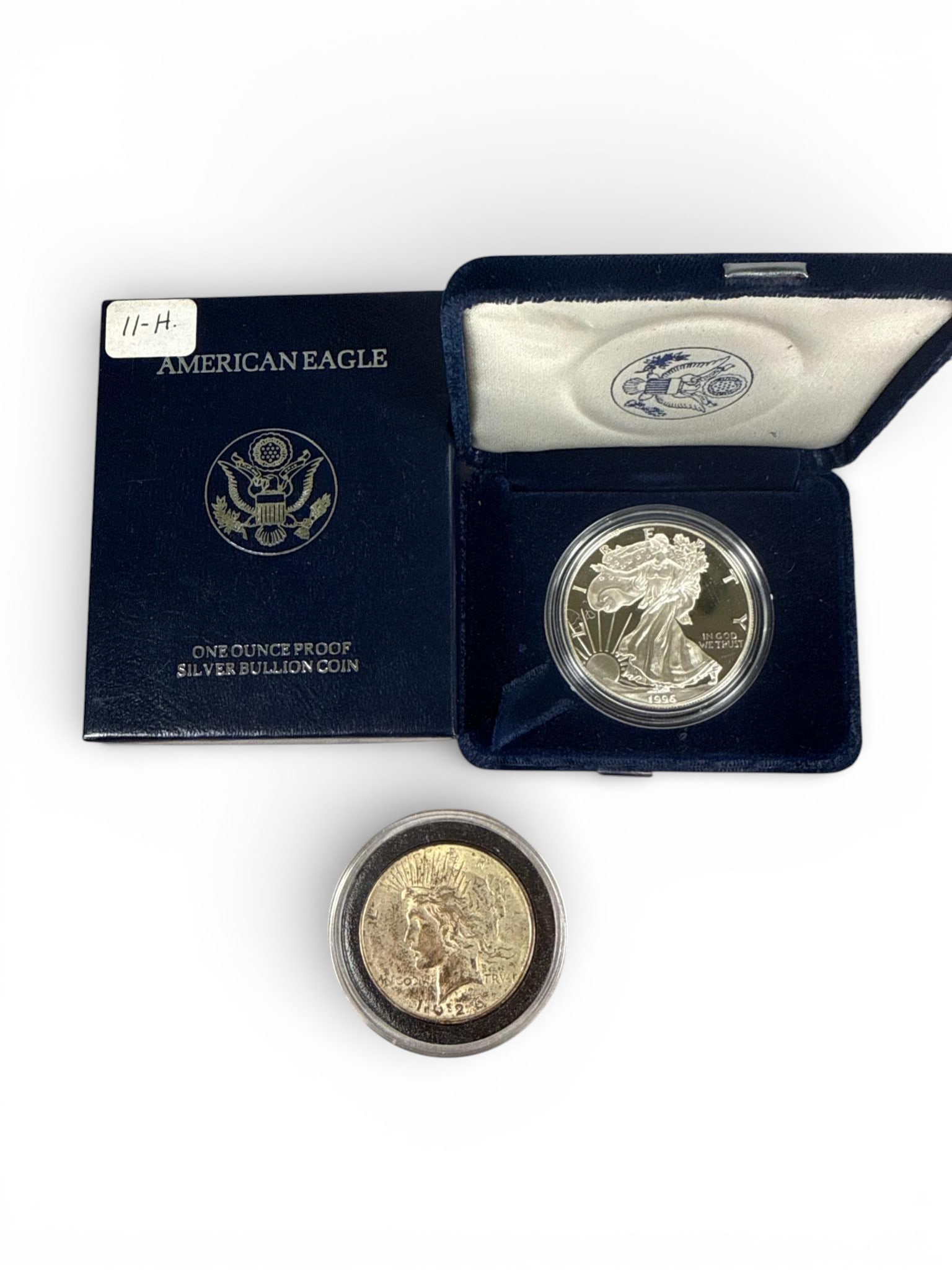 Two US Silver Coins Walking Liberty and Peace: A group of items centered around silver coins. The primary lot consists of a 1996 American Eagle A Ounce Proof Silver Bullion Coin, encapsulated in a clear plastic holder. The proof coin features the