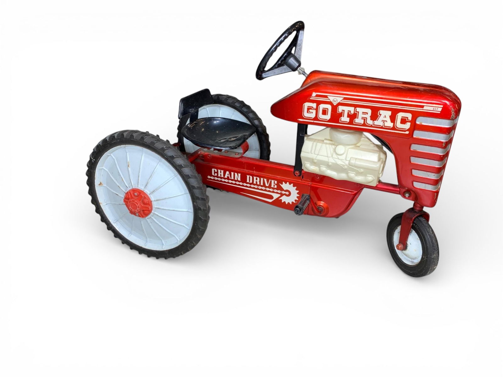GO TRAC Pressed Steel Chain Drive Pedal Tractor: A vintage child's ride-on pedal tractor, identified by the visible GO TRAC marking on the hood. The tractor is constructed primarily of red pressed steel with plastic and rubber components, characteri