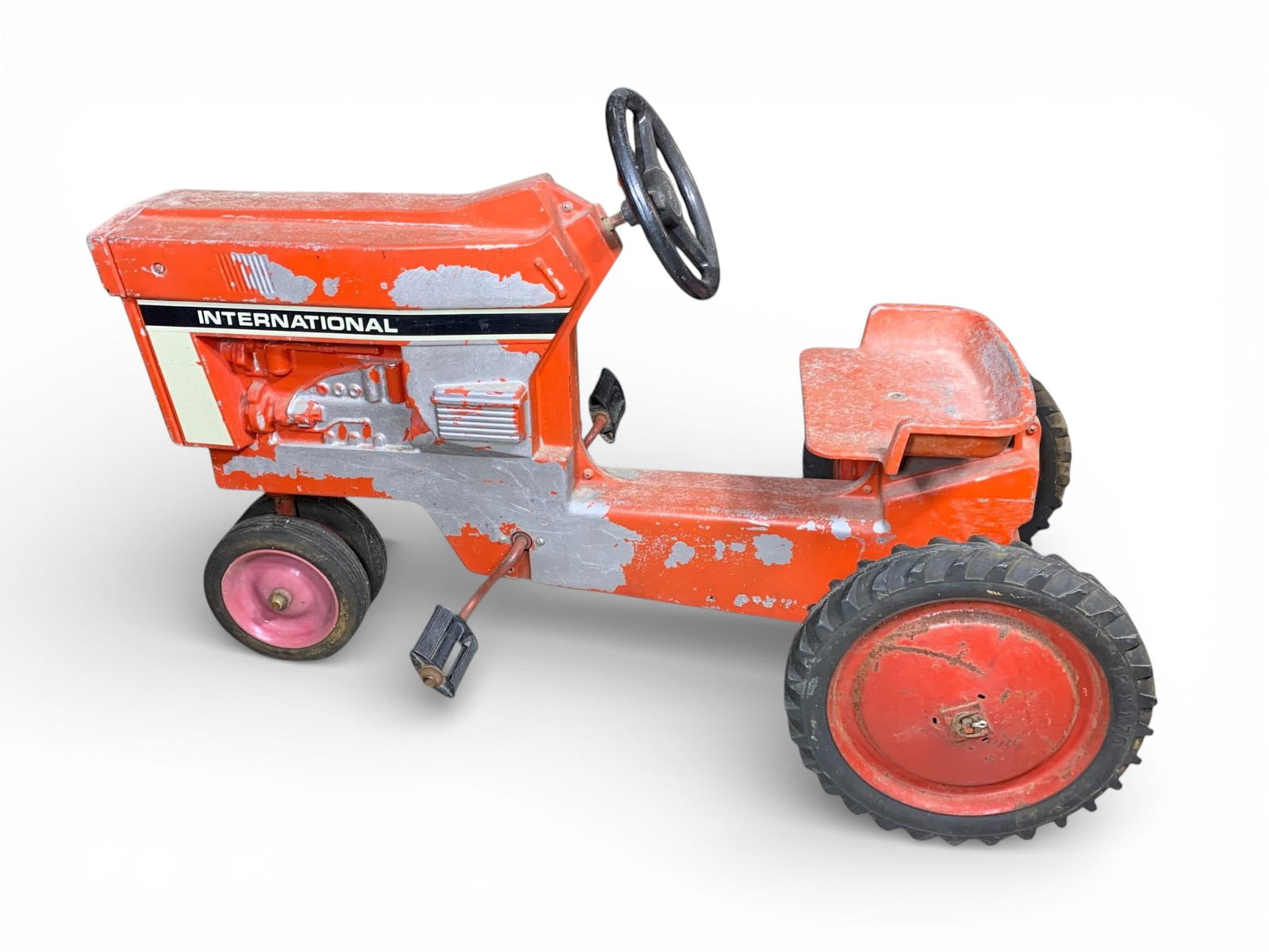 Vintage Ertl International Harvester Pedal Tractor: A vintage pedal tractor, attributed to Ertl and styled after an International Harvester agricultural vehicle. The body is constructed primarily of painted metal, finished in the characteristic orange/