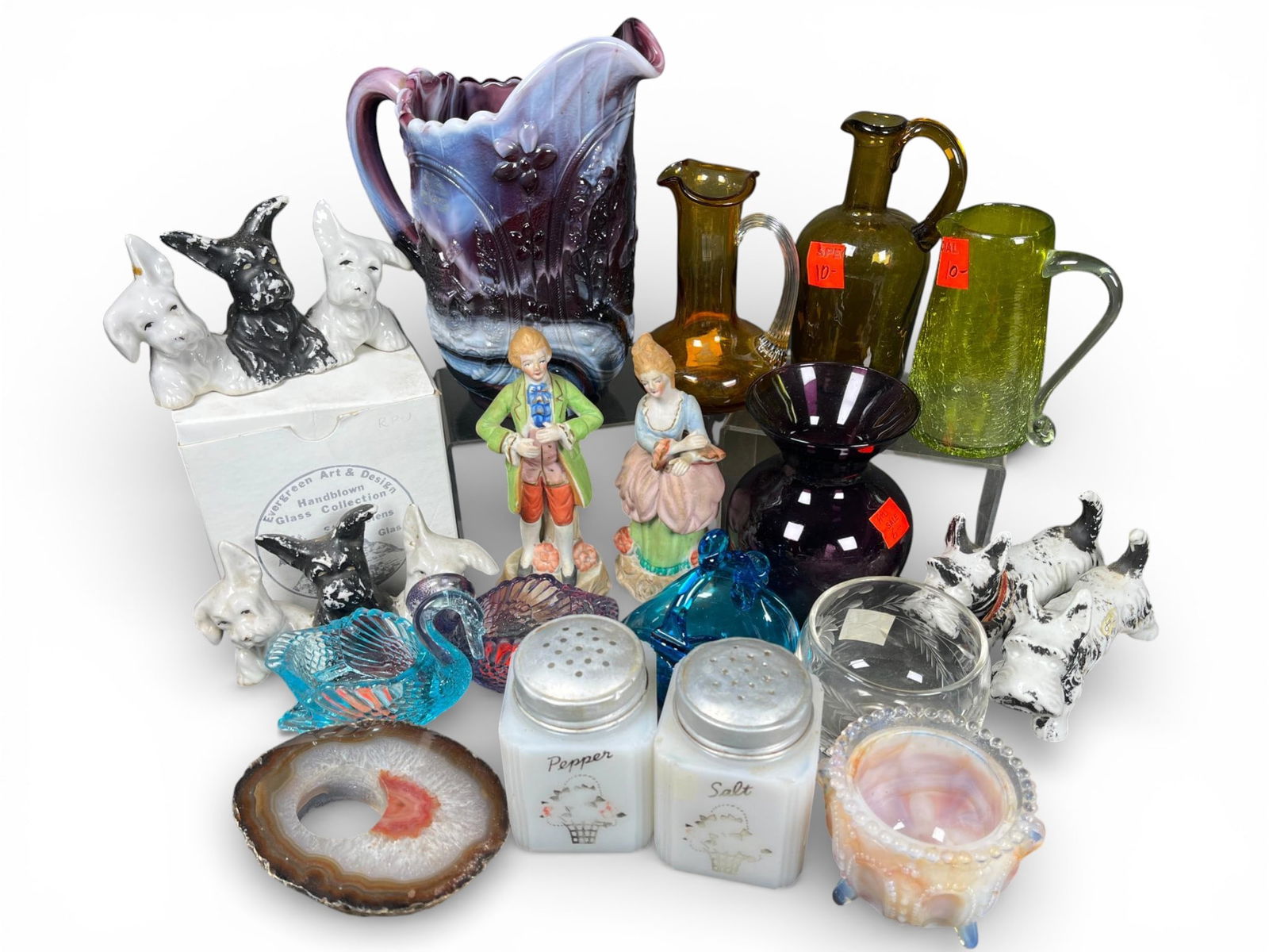 Decorative Objects Including Slag Glass Pitcher, Occupied Japan Figurines, and Pressed Glass: A group of miscellaneous decorative objects consisting of mixed glassware, porcelain figurines, and mineral specimens. The glassware includes a large purple and white marble glass (slag glass style)