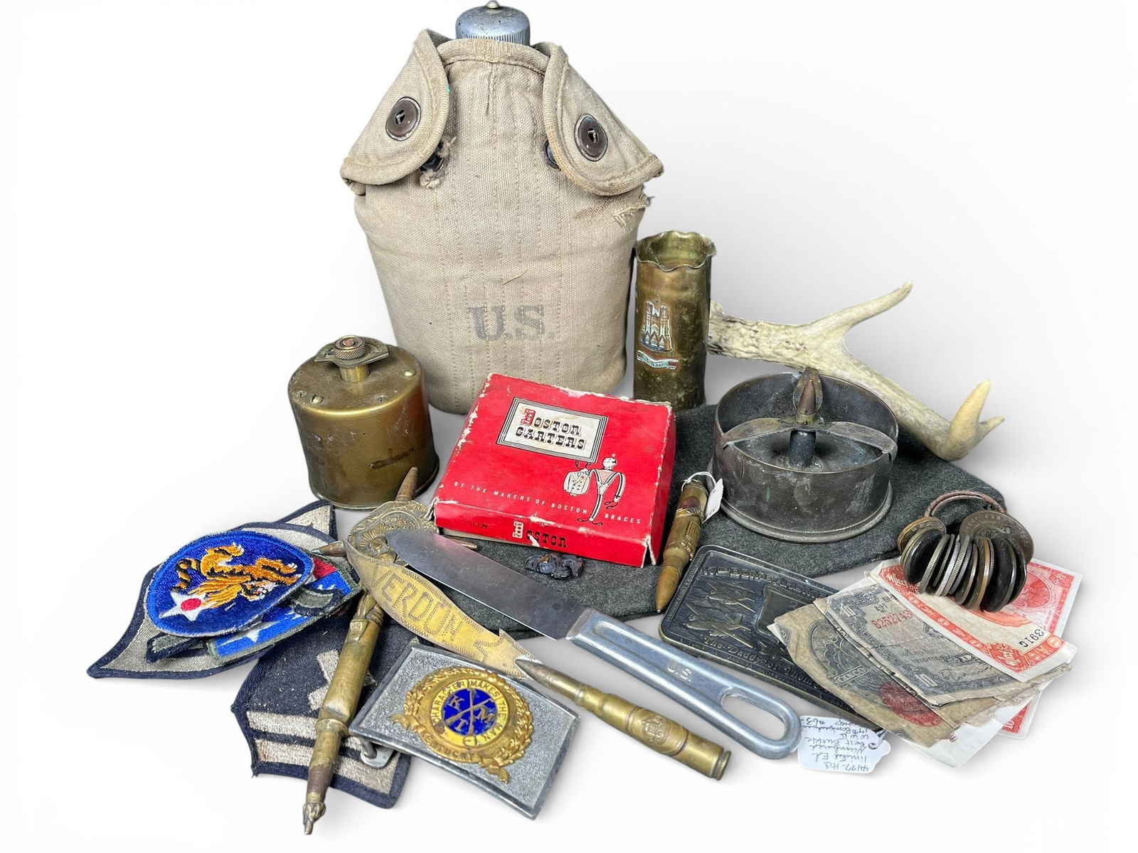 A group of Vintage Militaria, Knives, Canteen, and Currency: A group of items/groups of vintage militaria including a U.S. canteen, knives (a marked U.S. L.F.&C. 1945 and a marked VERDUN), a brass Reims shell casing vase, military buckles, a military cap,
