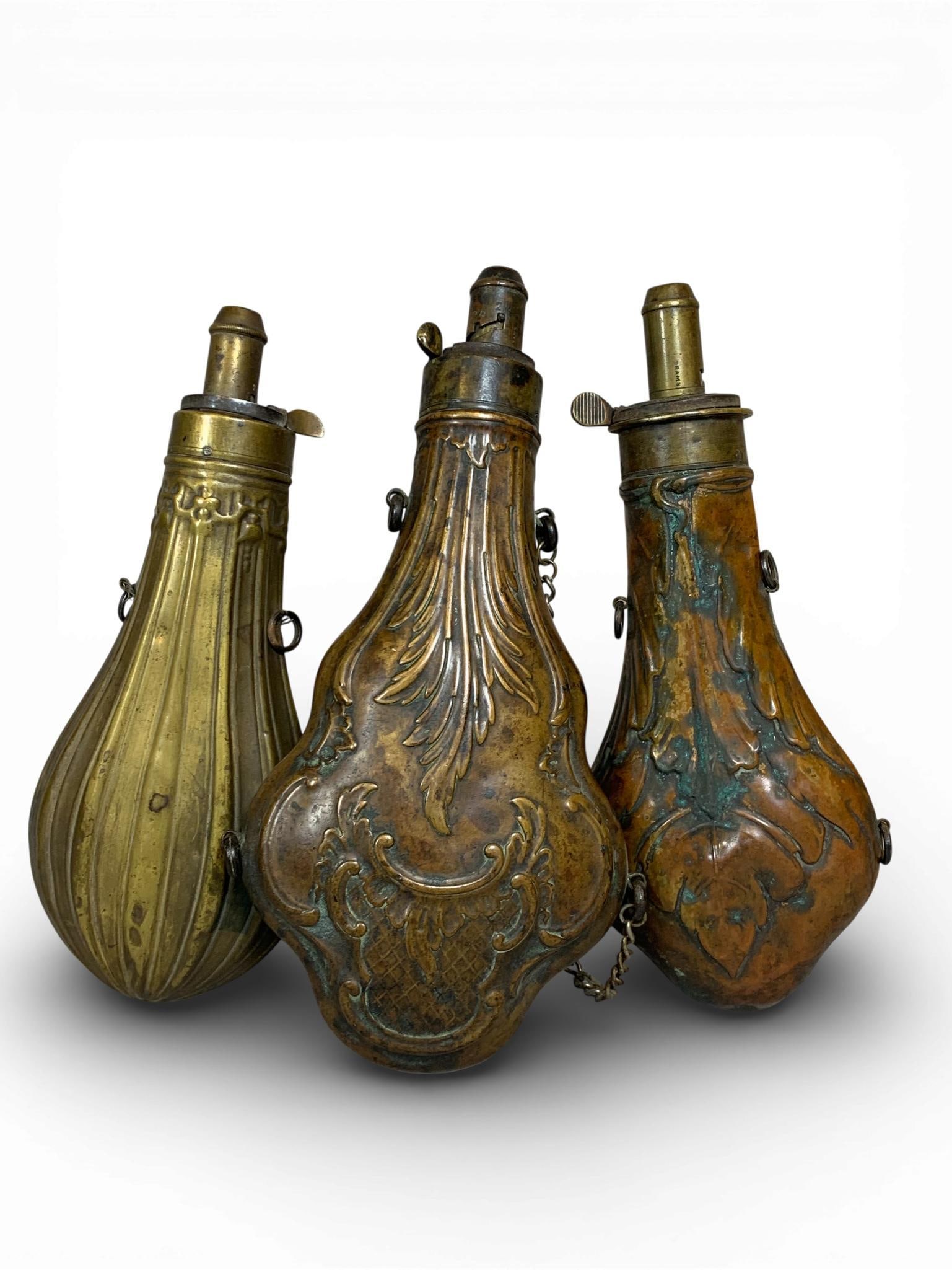 Three 19th Century Copper and Brass Powder Flasks by James Dixon and Sons, G. and J. W. Hawksley,: A trio of 19th-century powder flasks constructed from embossed copper and brass. The collection includes a flask by James Dixon and Sons of Sheffield featuring an embossed leaf motif and a graduated b
