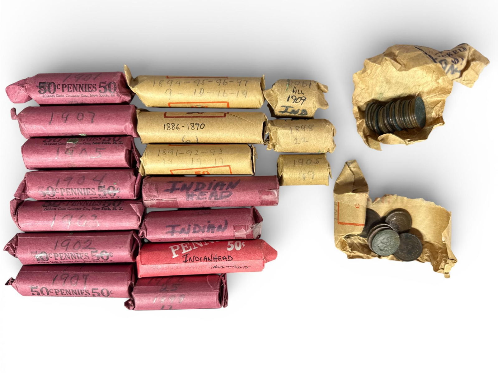 A Collection of Rolled United States Indian Head One-Cent Coins: A collection of rolled United States one-cent coins featuring the Indian Head motif. The coins are housed in a variety of red and tan paper wrappers. Several of the red wrappers are printed with 50c P