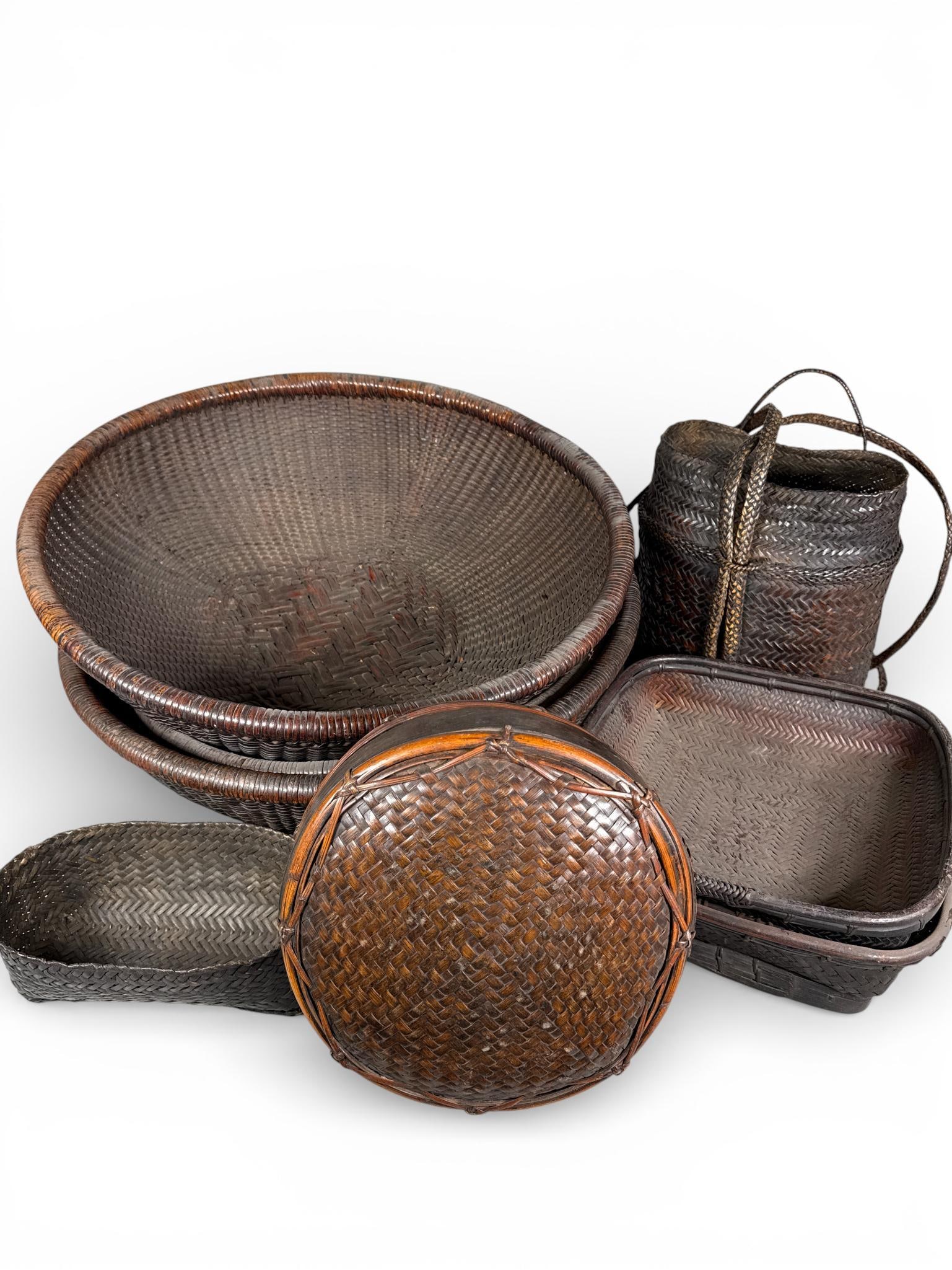 A Collection of Akha Thai and Southeast Asian Woven Rattan and Bamboo Baskets: A collection of Southeast Asian woven baskets, including examples attributed to the Akha people of Thailand. The group is constructed from dark-stained bamboo and rattan fibers utilizing traditional h