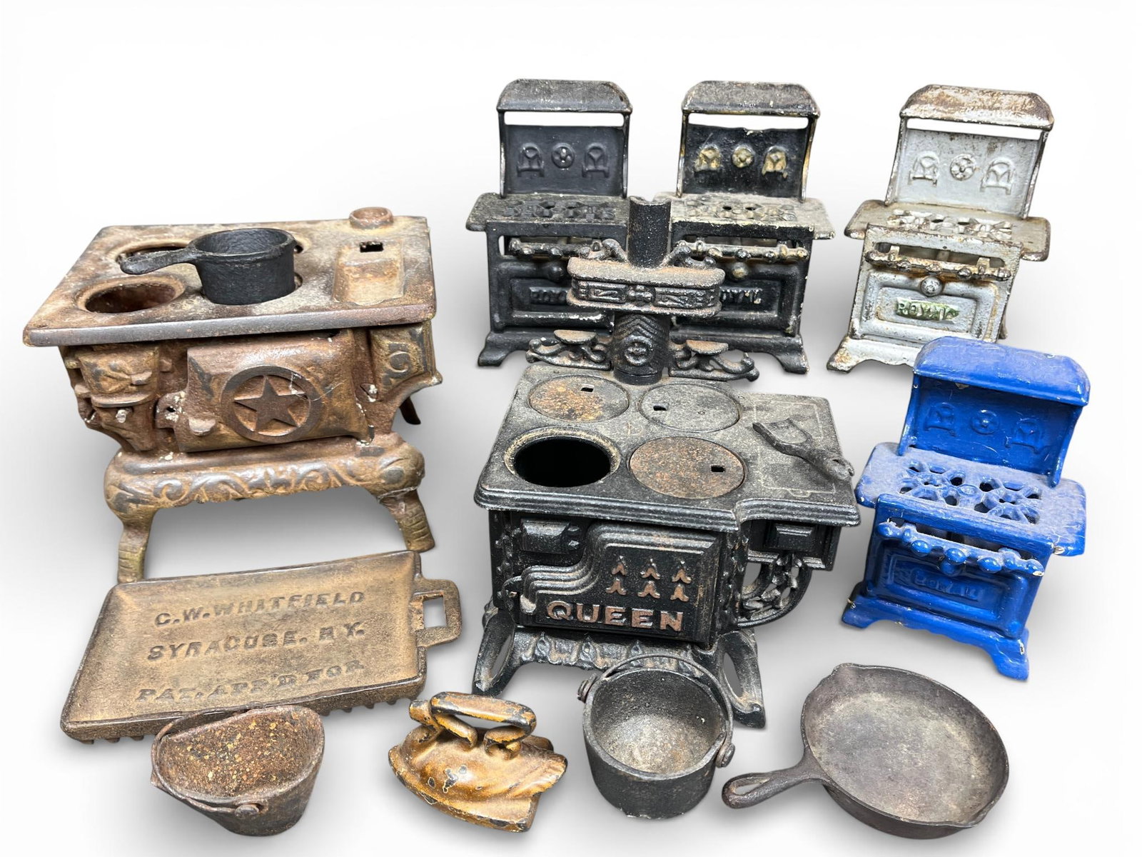 A Collection of Antique Crescent and Queen Miniature Cast Iron Stoves and Kitchen Accessories: A collection of late 19th to early 20th-century miniature and toy cast iron kitchen items, featuring stoves by Crescent and Queen. The group includes a black-finished Queen brand stove with removable