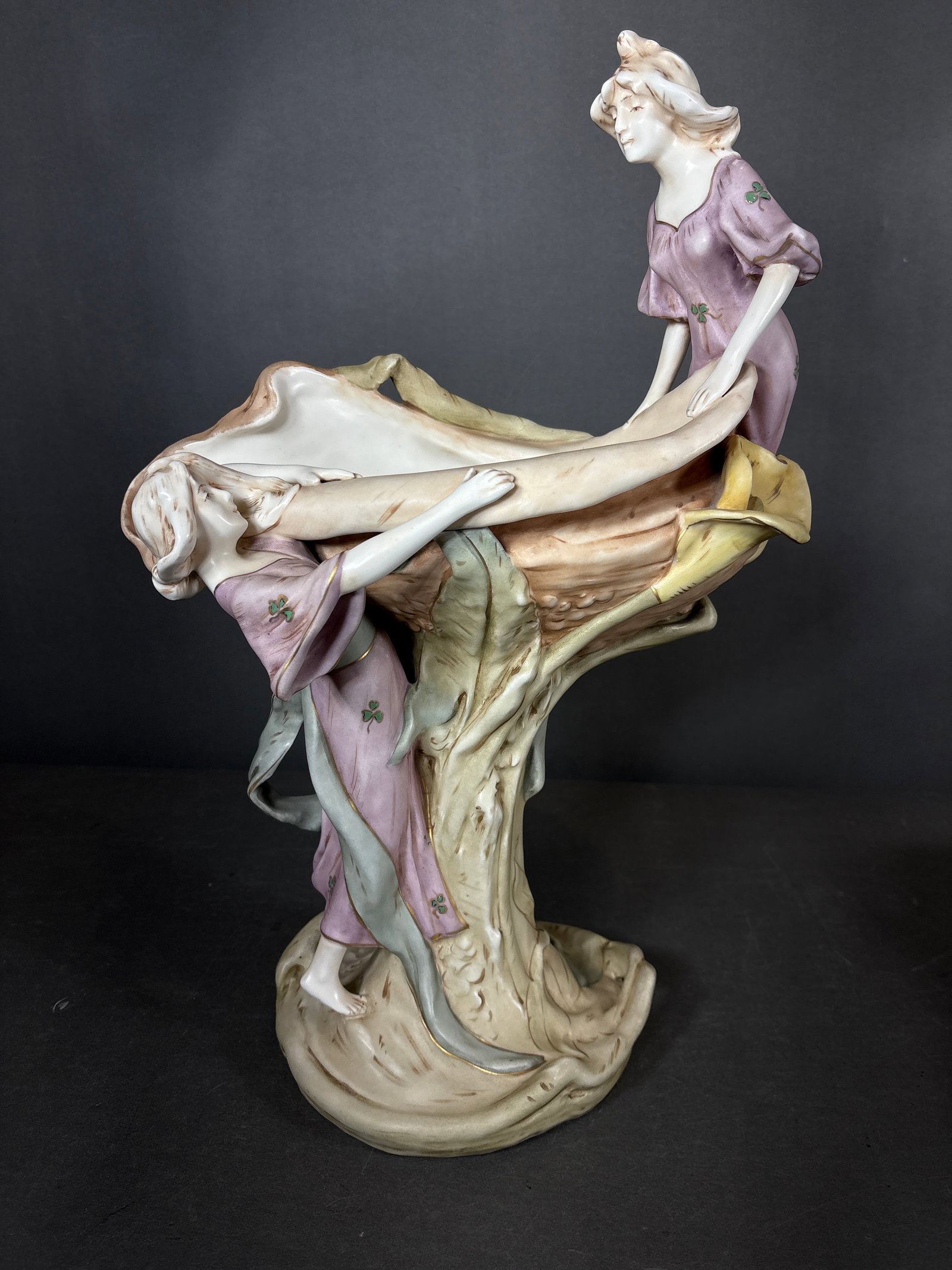 Royal Dux Art Nouveau Bohemian Glazed Porcelain Figural Centerpiece: This Royal Dux Art Nouveau style Bohemian glazed porcelain figural centerpiece features two female figures in flowing lavender gowns, each decorated with green trefoil motifs. The figures are position