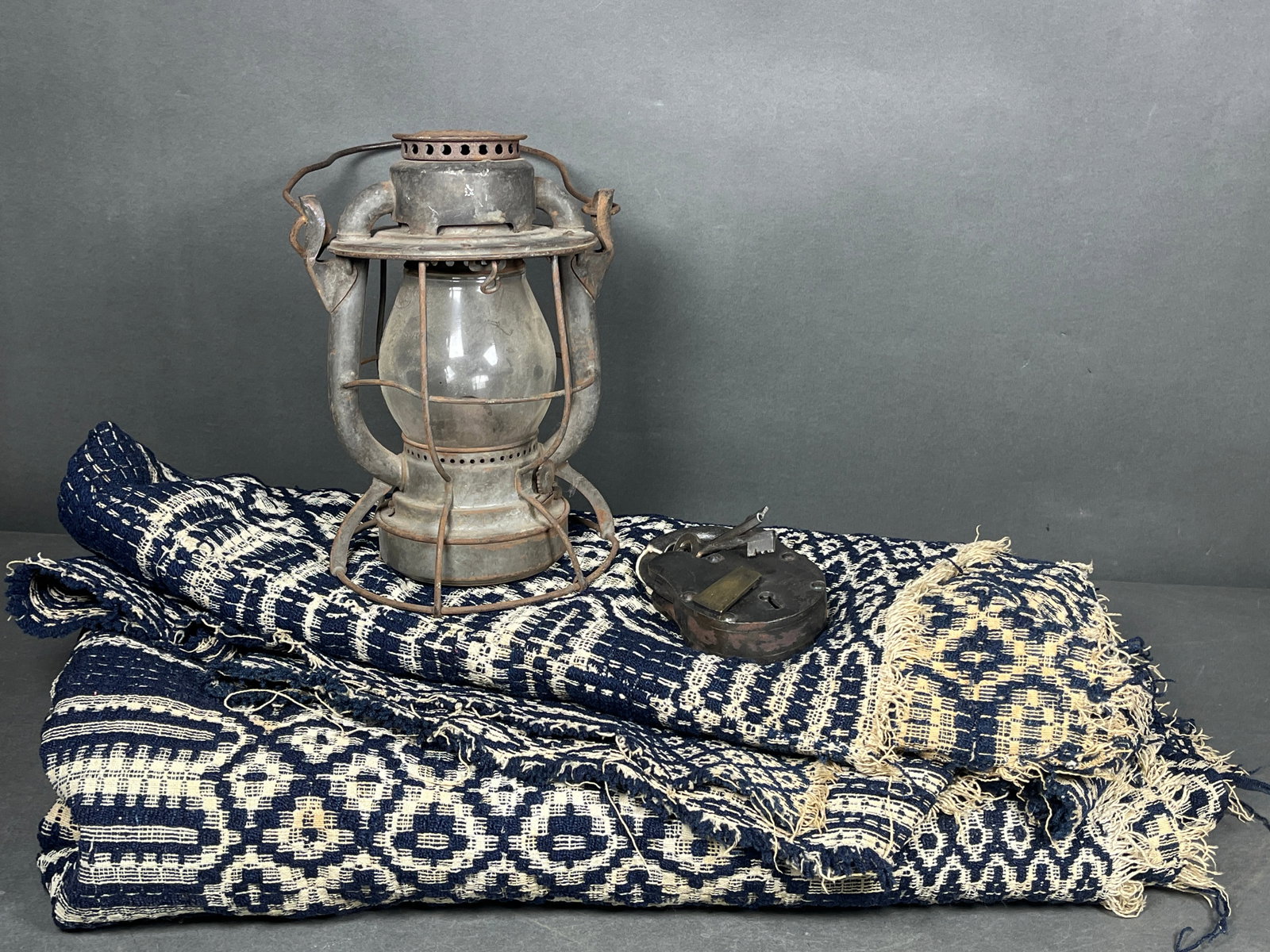 A Trio of Antique and Vintage Items Including a Dietz Vesta New York Central Railroad Lantern: A trio of antique and vintage items featuring a Dietz Vesta railroad lantern, a heavy-duty padlock, and a woven coverlet. The lantern is a Dietz Vesta model with embossed markings for NEW YORK