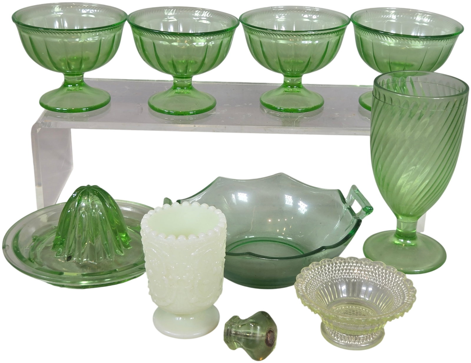 A Collection of Uranium and Custard Glass Tableware including Federal Glass and Fenton: A collection of Depression-era glassware, primarily composed of transparent green uranium glass that exhibits vibrant fluorescence under ultraviolet light. The group includes several footed dessert bo
