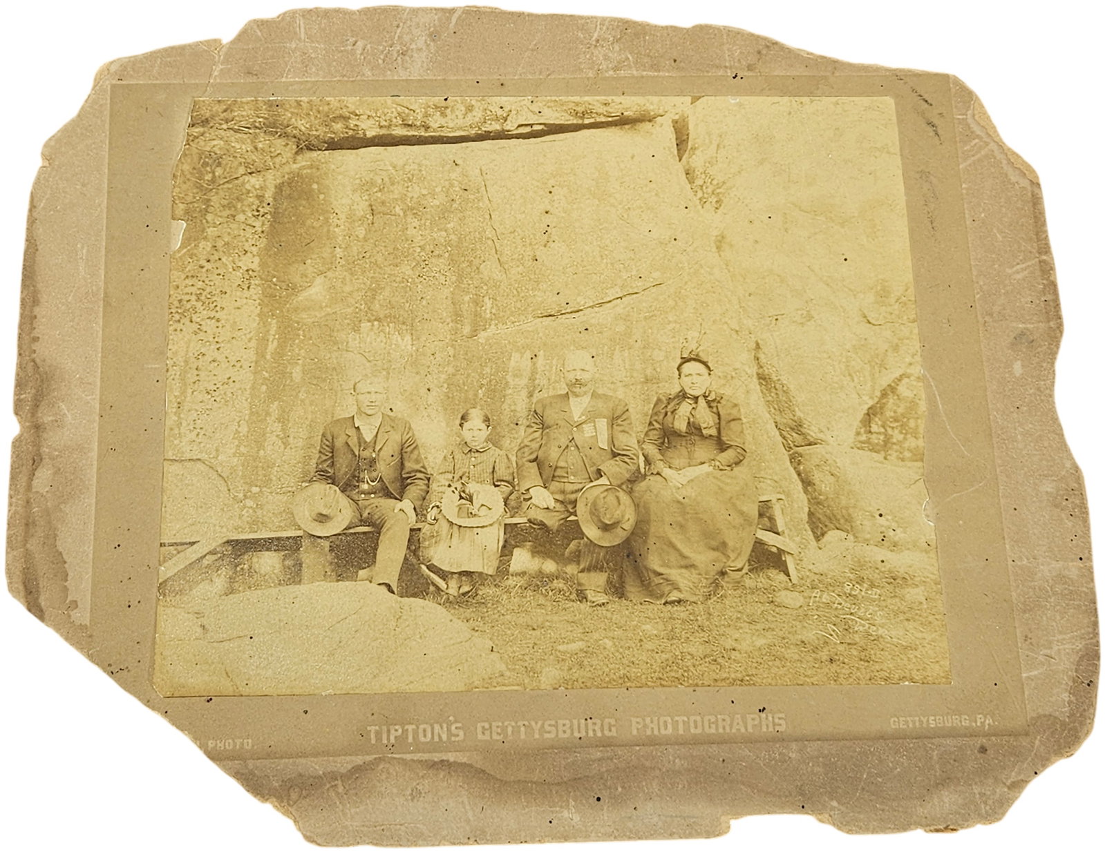 W.H. Tipton Albumen Print, Portrait of Andrew Jasper Jackson and Family at Gettysburg: This late 19th-century albumen print is mounted on a tan cardstock and depicts a group portrait of individuals seated on a simple wooden bench. The subjects are positioned against a massive rock face 