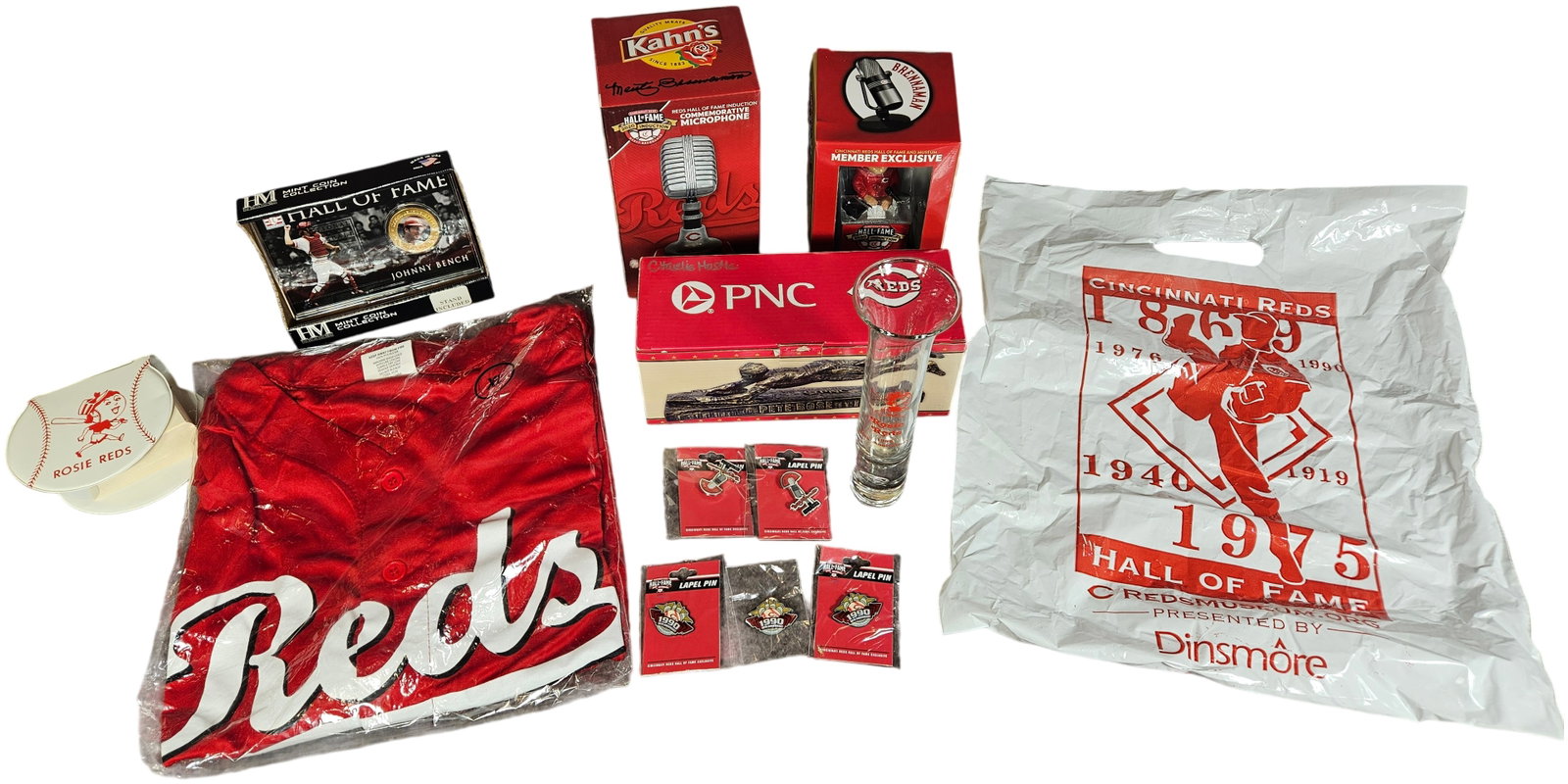 An Assortment of Cincinnati Reds Baseball Memorabilia and Collectibles including Pete Rose Statue: A collection of Cincinnati Reds baseball memorabilia and promotional items. The group includes a red polyester baseball jersey, size XL, featuring the team name in white script on the front and the nu