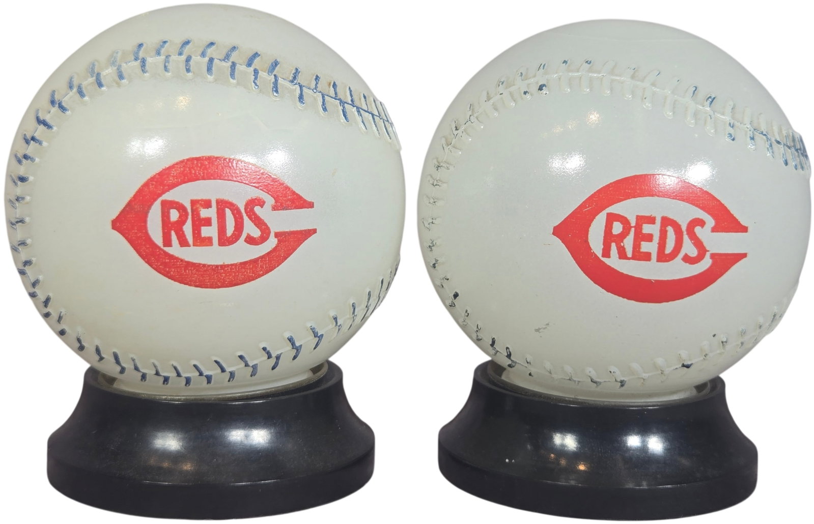 A Pair of Vintage Cincinnati Reds and Mobilgas Promotional Baseball Coin Banks: A pair of vintage promotional baseball-themed coin banks constructed of white plastic with blue printed decorative stitching. A side of each bank features the Cincinnati Reds logo, comprised of a red 
