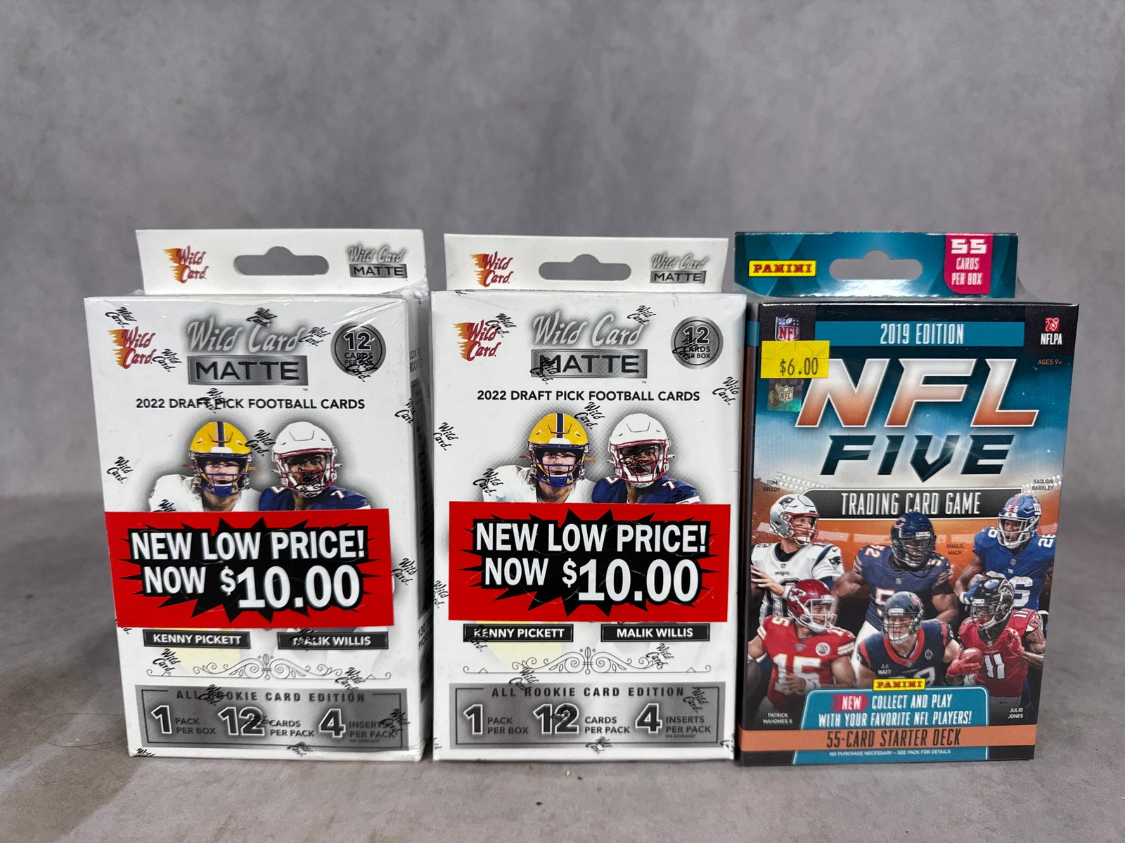 Factory-Sealed Football Trading Card Boxes Including 2022 Wild Card Matte Draft Pick and 2019 Panini: This lot consists of factory-sealed football trading card boxes. Included are two 2022 Wild Card Matte Draft Pick Football hanger boxes and one 2019 Panini NFL a group of Trading Card Game starter dec