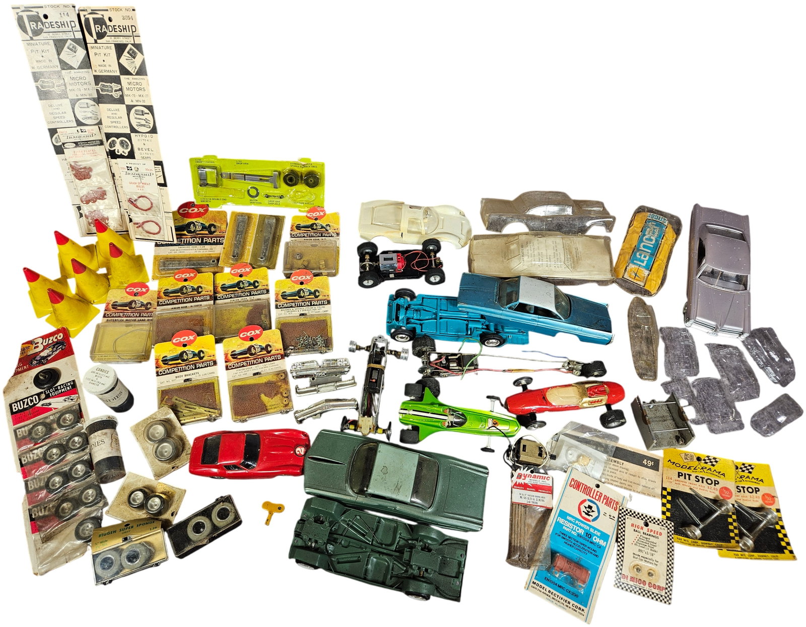 A Collection of Vintage 1/24 and 1/32 Scale Slot Car Parts, Bodies, and Accessories by Cox, K&B, and: An assortment of vintage slot car components, accessories, and vehicle bodies in 1/24 and 1/32 scales, primarily dating to the 1960s. The lot includes items constructed from die-cast metal, plastic, a
