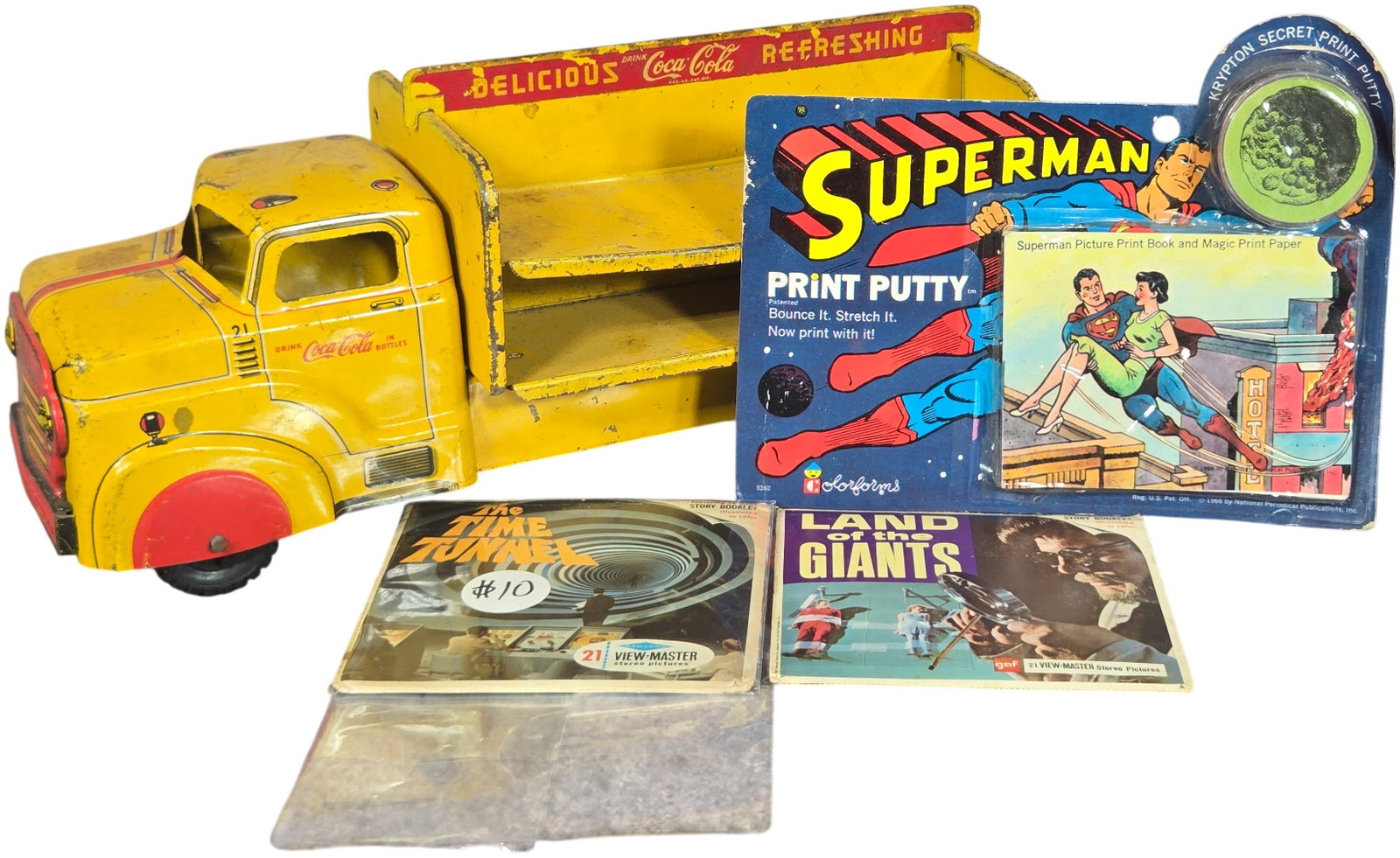 A Collection of Vintage 1960s Toys Including Marx Coca-Cola Truck and Superman Print Putty: This collection features an assortment of toys and memorabilia from the 1960s. Included is a Marx Toys (Louis Marx and Co.) pressed steel Coca-Cola delivery truck. The yellow truck body features open 