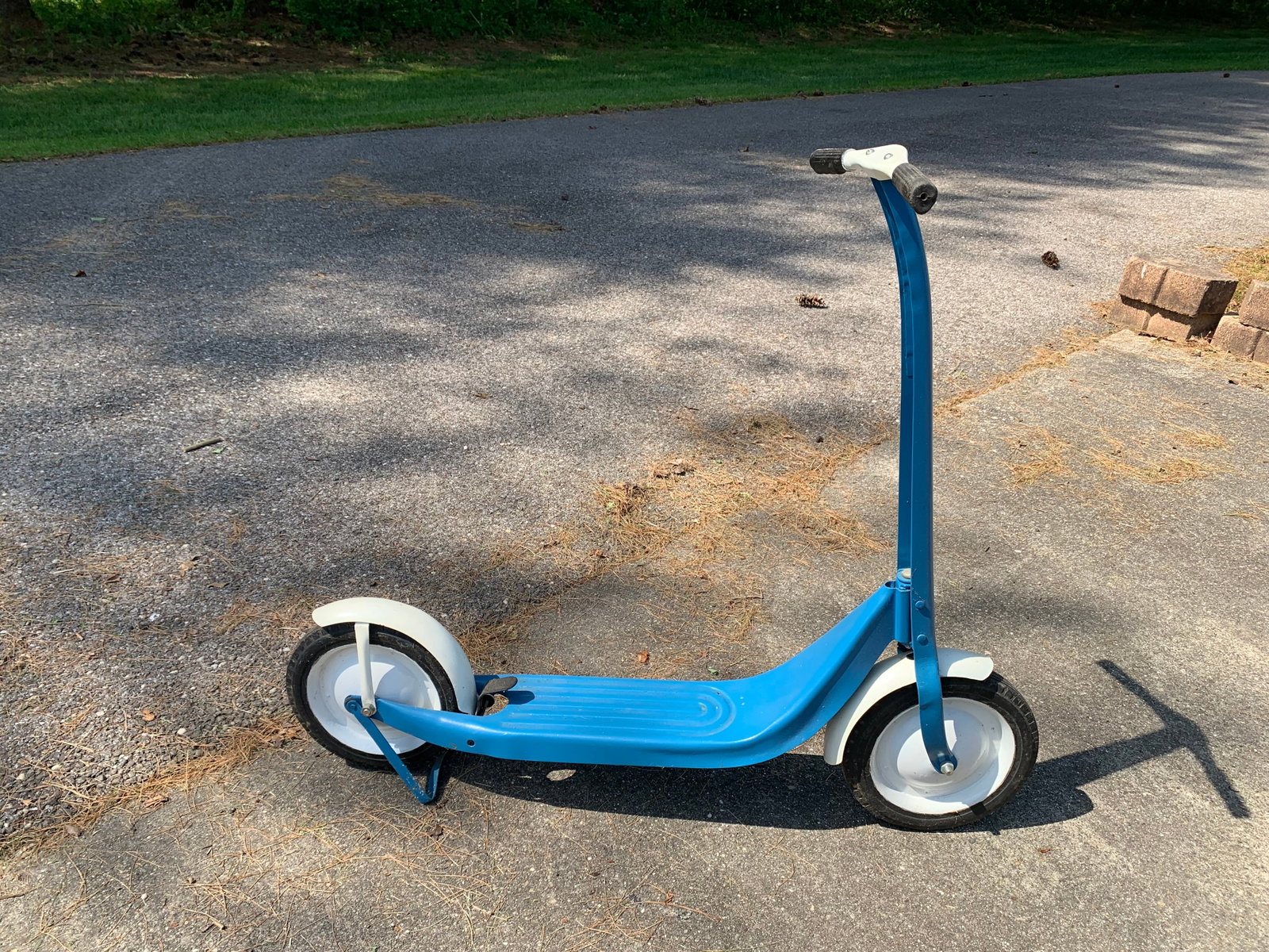 Vintage Children's Kick Scooter attributed to Radio Line or Western Chief: This vintage children's manual kick scooter is a streamlined mid-century toy. The frame and body are constructed of pressed steel with a blue and white painted finish. The design features a curved upr