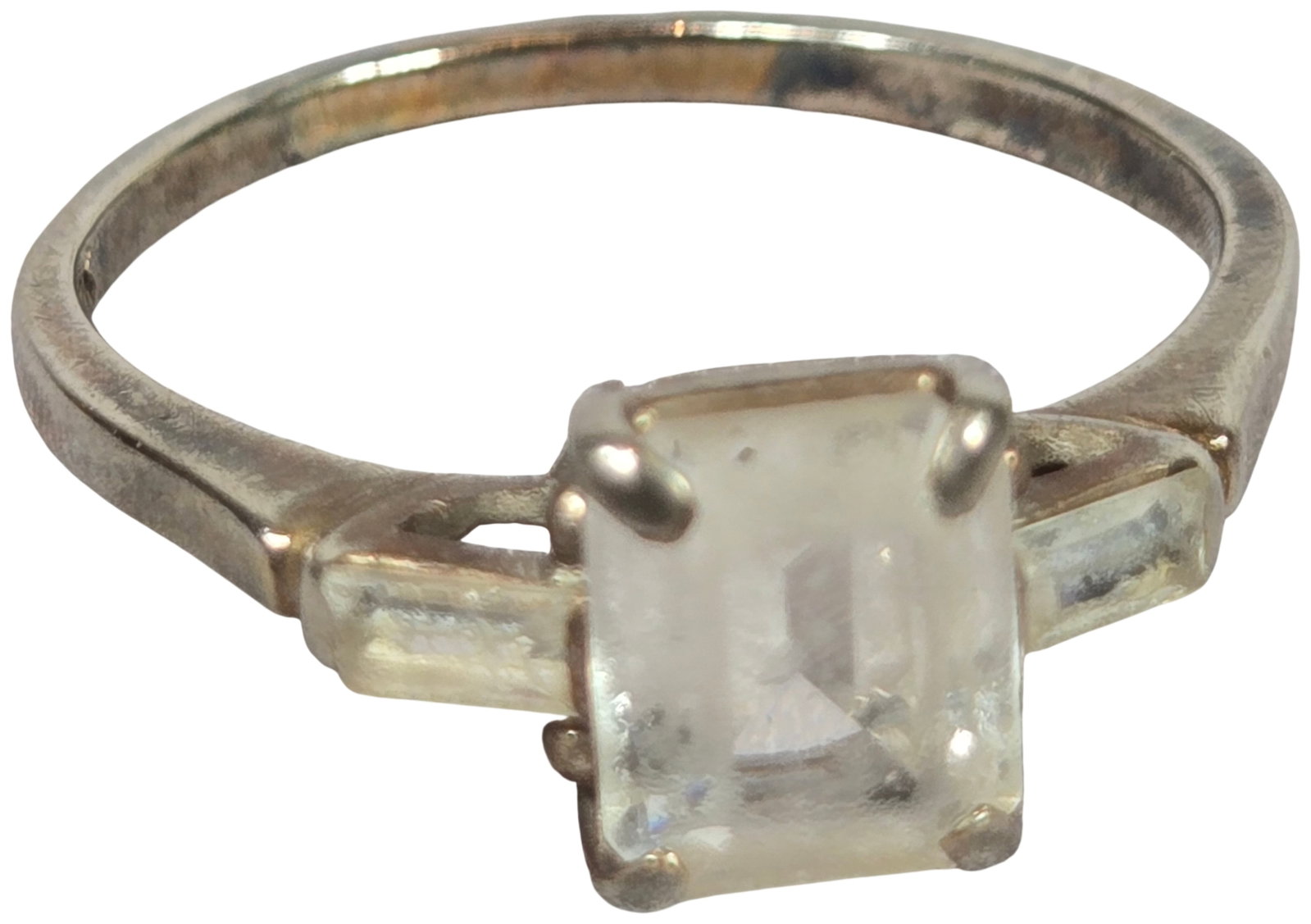 10K White Gold Three-Stone Ring with Emerald Cut and Baguette Colorless Gemstones: A 10-karat white gold ring in a three-stone cocktail design. The center setting holds a single emerald-cut colorless gemstone, measuring approximately 8mm by 6mm, secured by four prongs. The