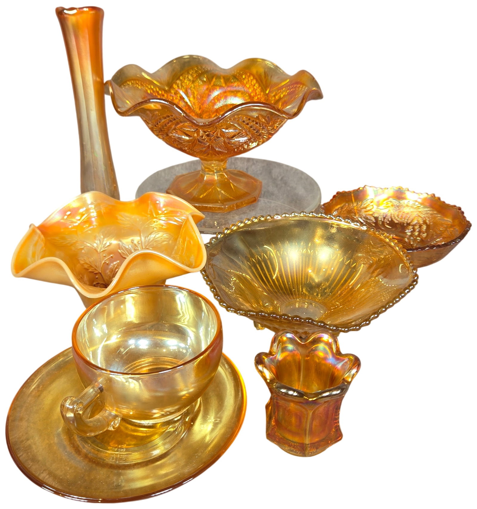 An Assortment of Marigold Carnival Glass Tableware: This assortment of American marigold carnival glass features pressed glass with a metallic iridescent finish. The collection includes a variety of decorative and functional forms common to early 20th-