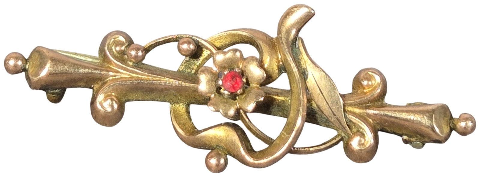 Edwardian 9 Karat Yellow Gold Bar Brooch with Red Gemstone by Sydenham Brothers 1906: An antique Edwardian-style bar brooch manufactured by Sydenham Brothers. The piece is constructed from 9 karat yellow gold and features a central floral motif with six petals, prong-set with a single 