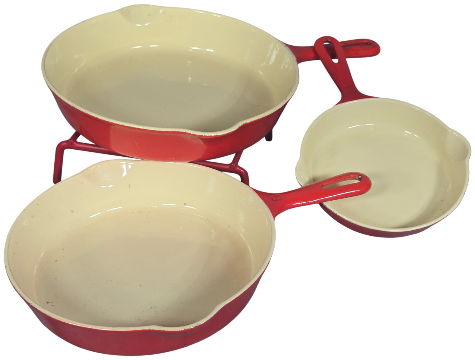 A Trio of Griswold 100th Anniversary Enameled Cast Iron Skillets with Rack: A set of three graduated commemorative skillets with a matching wire display rack, manufactured by Griswold. The items are constructed from cast iron featuring a vibrant red exterior enamel and a crea