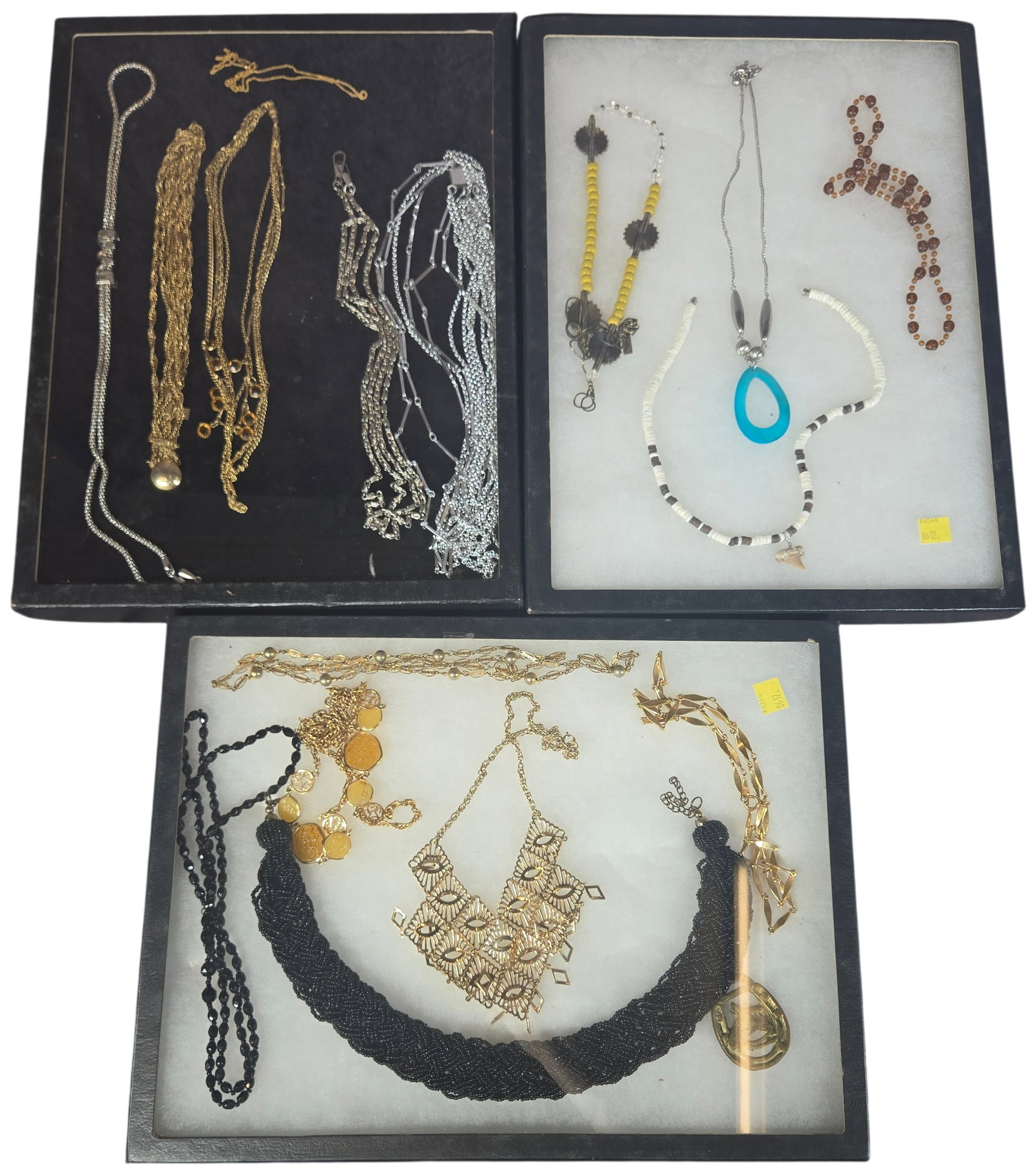 Assorted costume jewelry collection.: Cases not included. This lot comprises fourteen assorted costume jewelry necklaces and pendants presented in three black-framed glass-top display cases. The collection features a variety of styles, ma