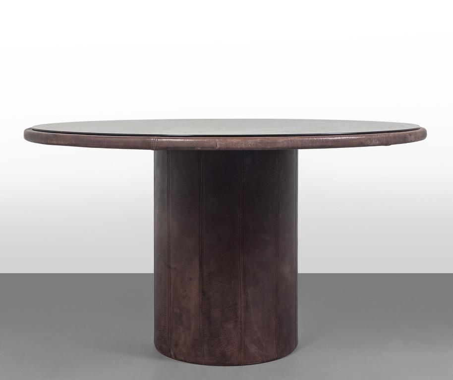 DE SEDE (Editore) Un tavolo, anni '70.: DE SEDE (Editore) Un tavolo, anni '70. Supporto centrale di legno rivestito in pelle, piano di cristallo bronzato argentato. Altezza cm 72, diametro cm 130.