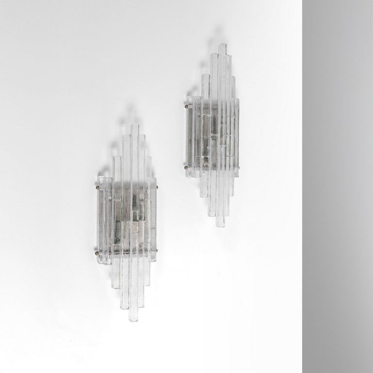 POLIARTE (Editore), anni '70. Due lampade da: POLIARTE (Editore), anni '70. Due lampade da parete. Strutture in acciaio inox satinato, barre di cristallo. Cm 49 (h) x 16 (l) x 8 (p).