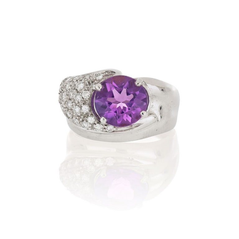 Anello in oro bianco di moderna lavorazione,: Anello in oro bianco di moderna lavorazione, un'ametista taglio ovale è arricchita da un pavè di diamanti taglio brillante, montati a formare una fiamma stilizzata su un lato, ct. 0,60 ca. M