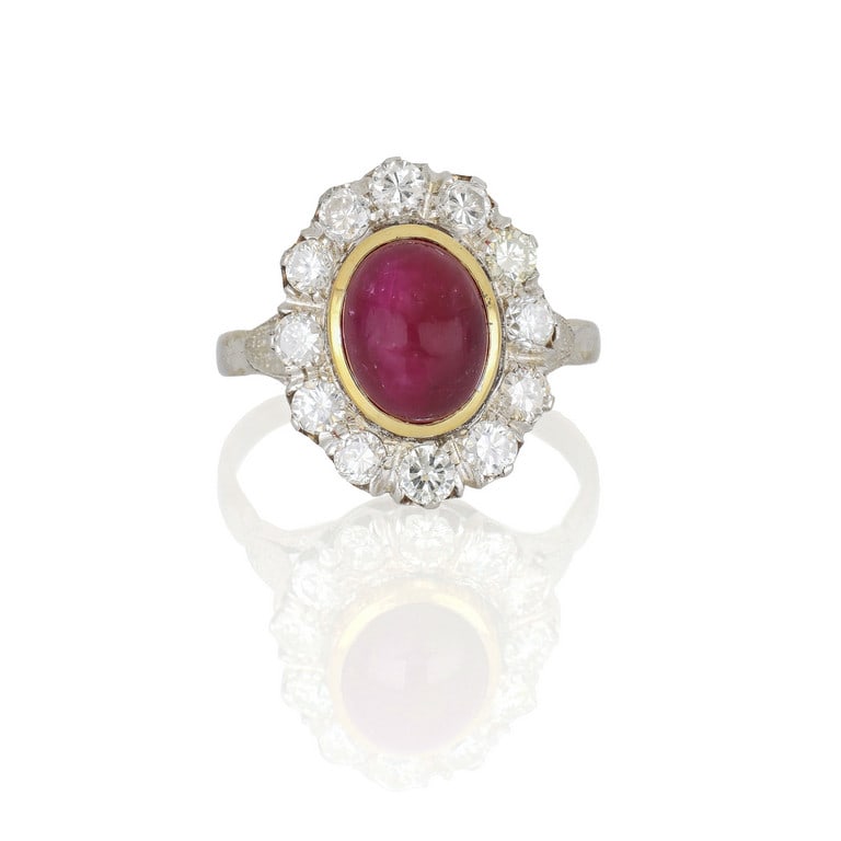 Anello a margherita in oro bianco e giallo, al: Anello a margherita in oro bianco e giallo, al centro un rubino taglio ovale cabochon di ct. 3,00 ca. e diamanti taglio brillante a contorno per ct. 1,00 ca. Misura n. 18. Peso 5,56 g.