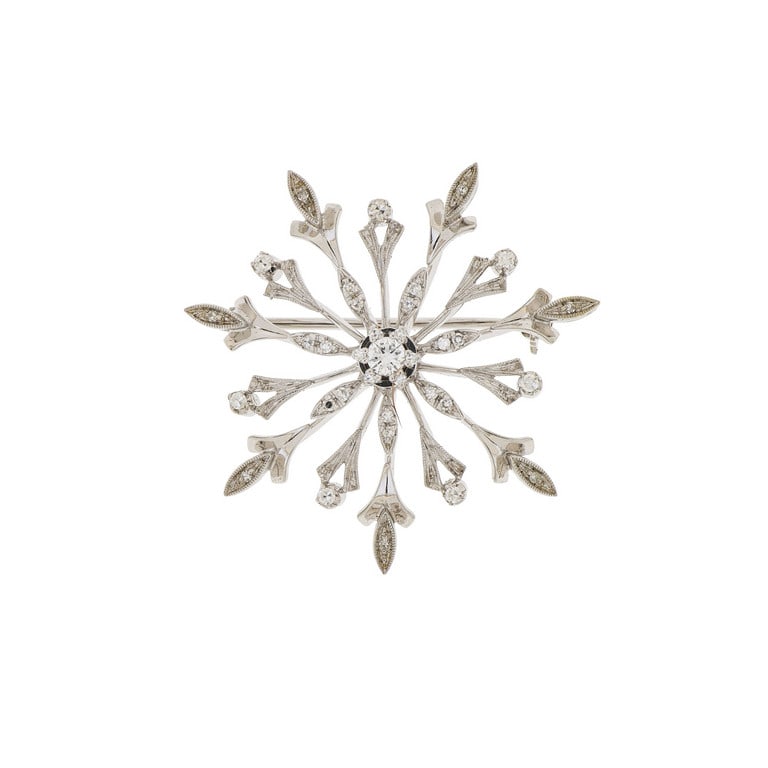 Spilla in oro bianco a fiocco di neve, al centro: Spilla in oro bianco a fiocco di neve, al centro un diamante taglio brillante di ct. 0,20 ca., altri piccoli a decorare il gioiello. Diametro 4 cm. Peso 9,15 g.