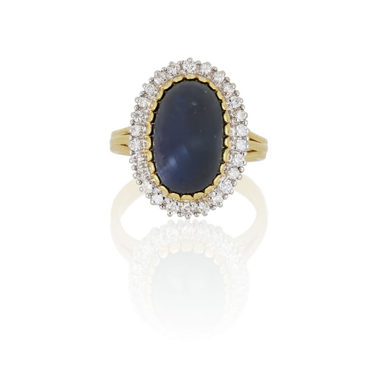 Anello di forma ovale in oro giallo e bianco, un: Anello di forma ovale in oro giallo e bianco, un grande zaffiro taglio cabochon, ct. 6,00 ca. è finemente contornato da piccoli diamanti taglio brillante per ct. 0,50 ca. Misura n. 11. Peso 9,23 